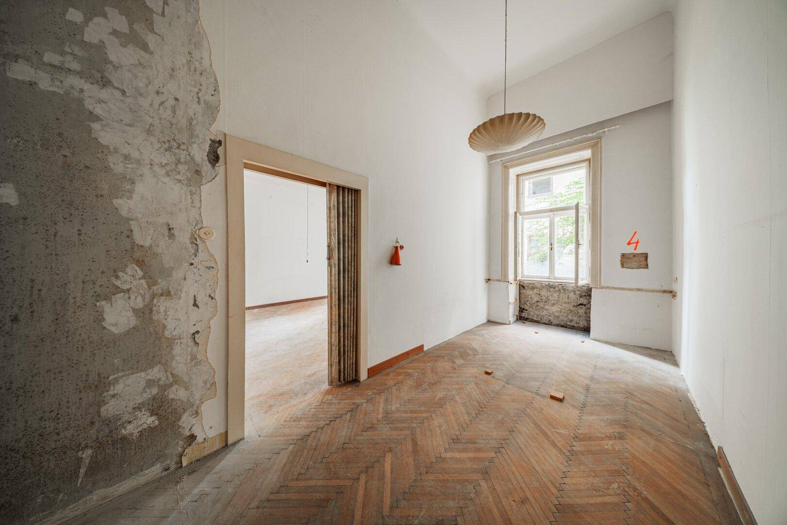 Helles Zimmer mit Fischgrätparkett und großem Fenster, ideal für eine Neugestaltung.