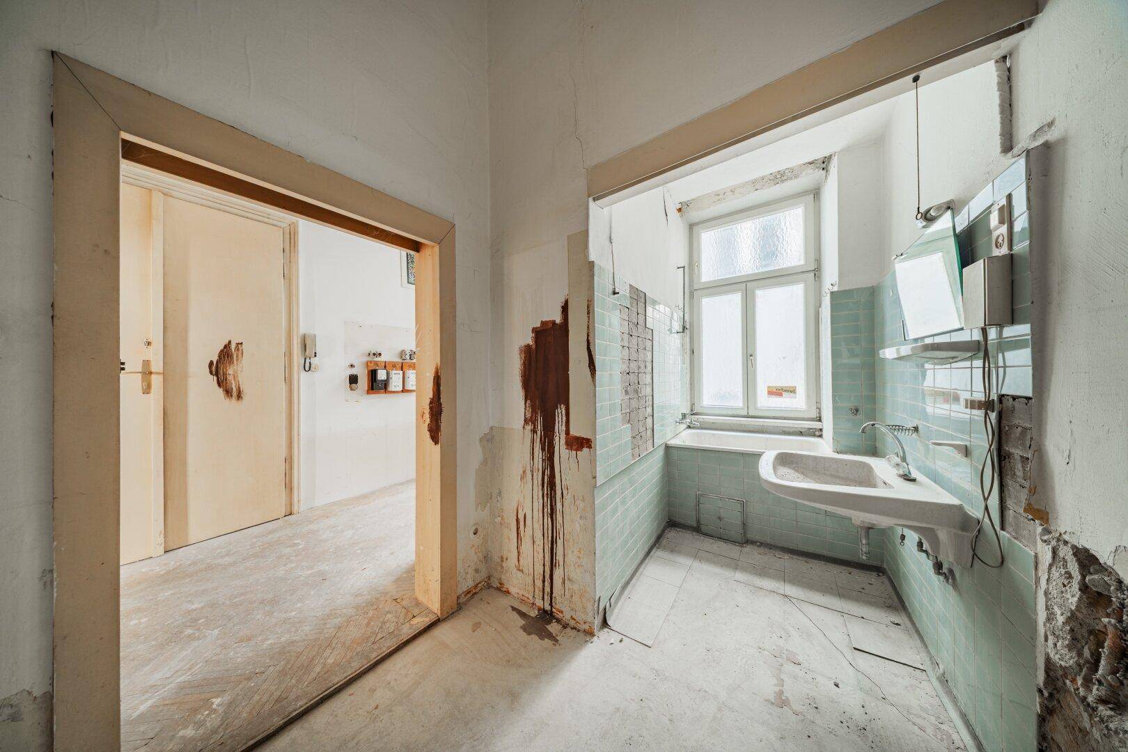 Badezimmer in Renovierung mit alten grünen Fliesen, Waschbecken und Fenster, das auf eine Modernisierung wartet.