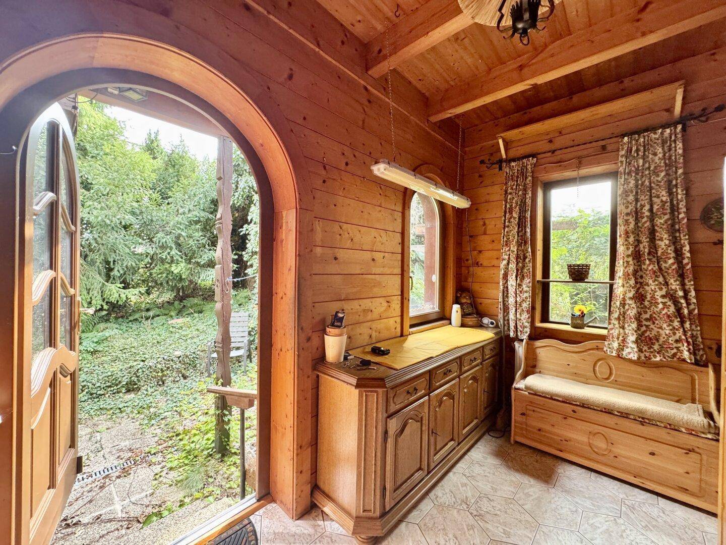 Gemütlicher Eingangsbereich mit Holzwänden, Holzboden und Blick ins Grüne durch die offene Tür.