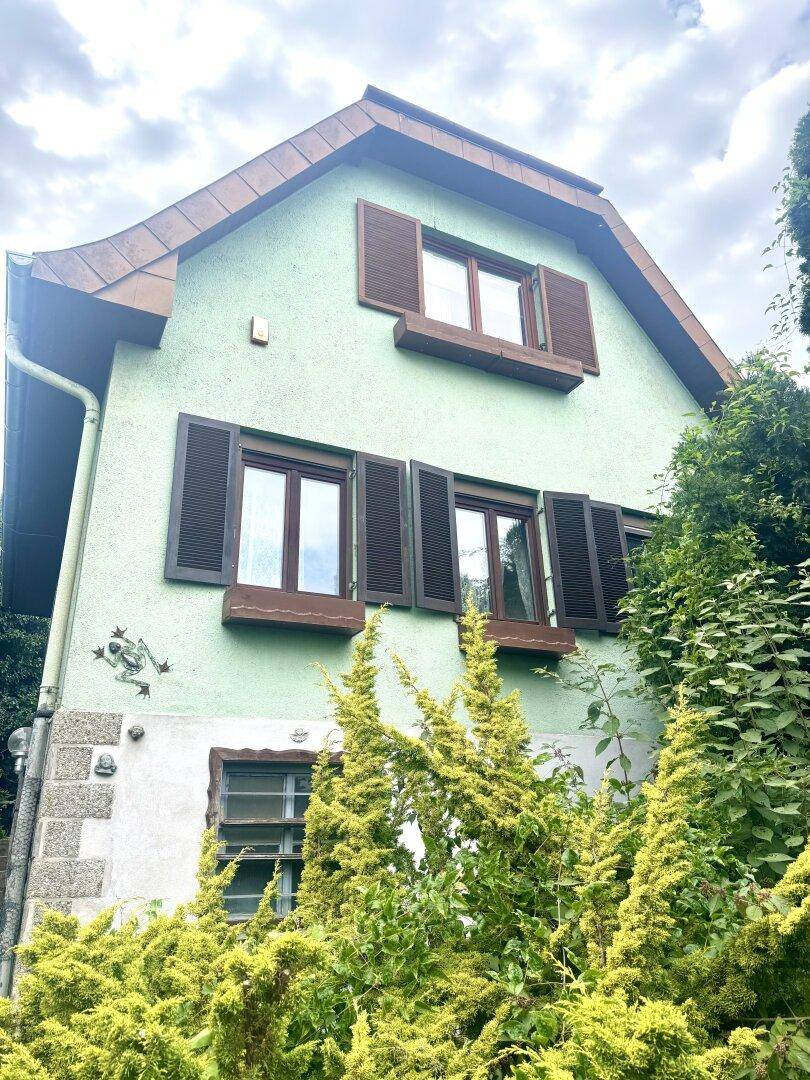 Detailansicht der hellgrünen Hausfassade mit braunen Fensterläden und dekorativen Elementen.