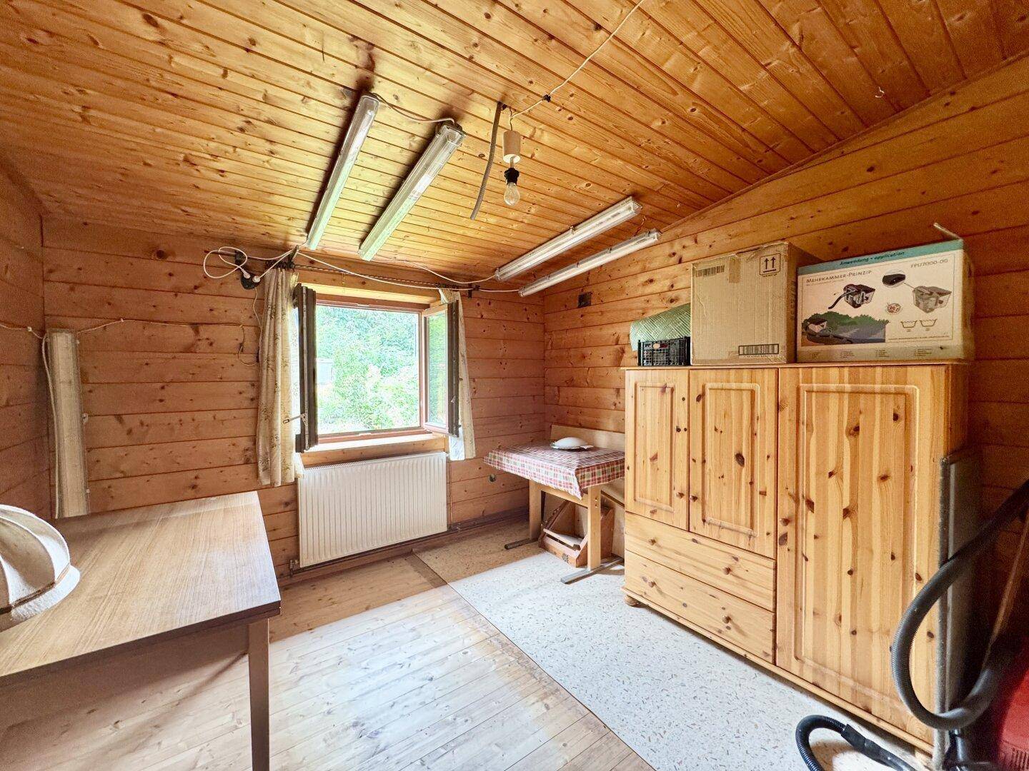 Rustikales Zimmer mit Holzwänden, Holzboden und einem Fenster, das viel Tageslicht hereinlässt.