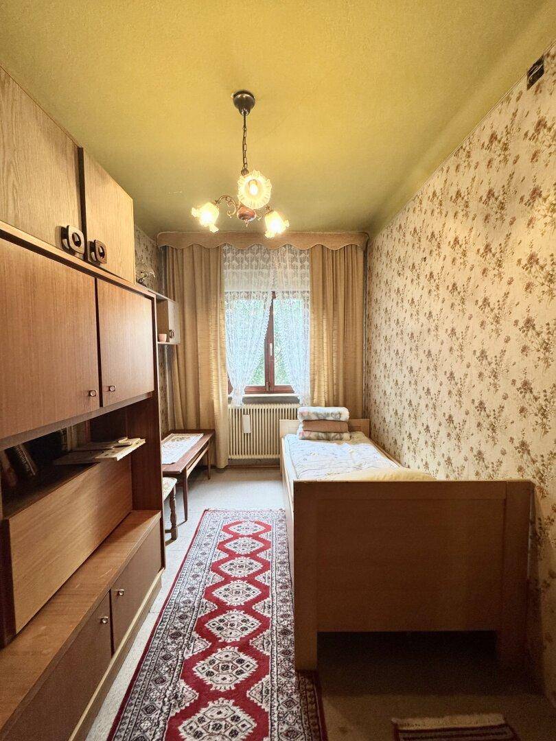 Schlafzimmer im traditionellen Stil mit floraler Tapete, Einzelbett und Teppichboden.