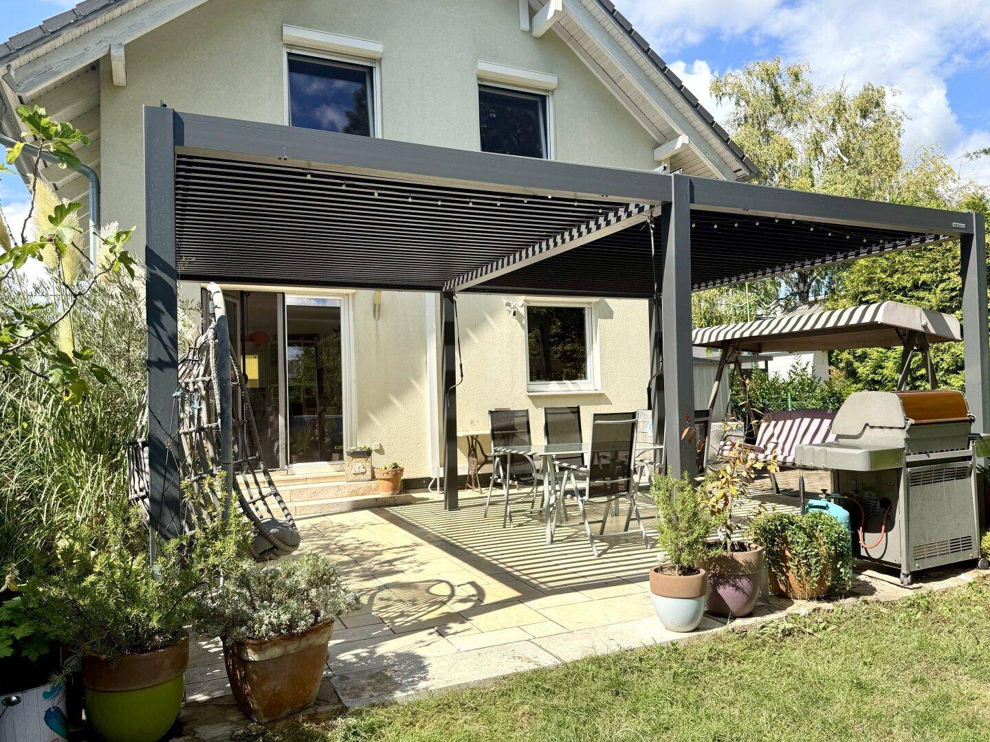 Überdachte Terrasse mit modernen Gartenmöbeln und Grillbereich, ideal für entspannte Stunden im Freien.