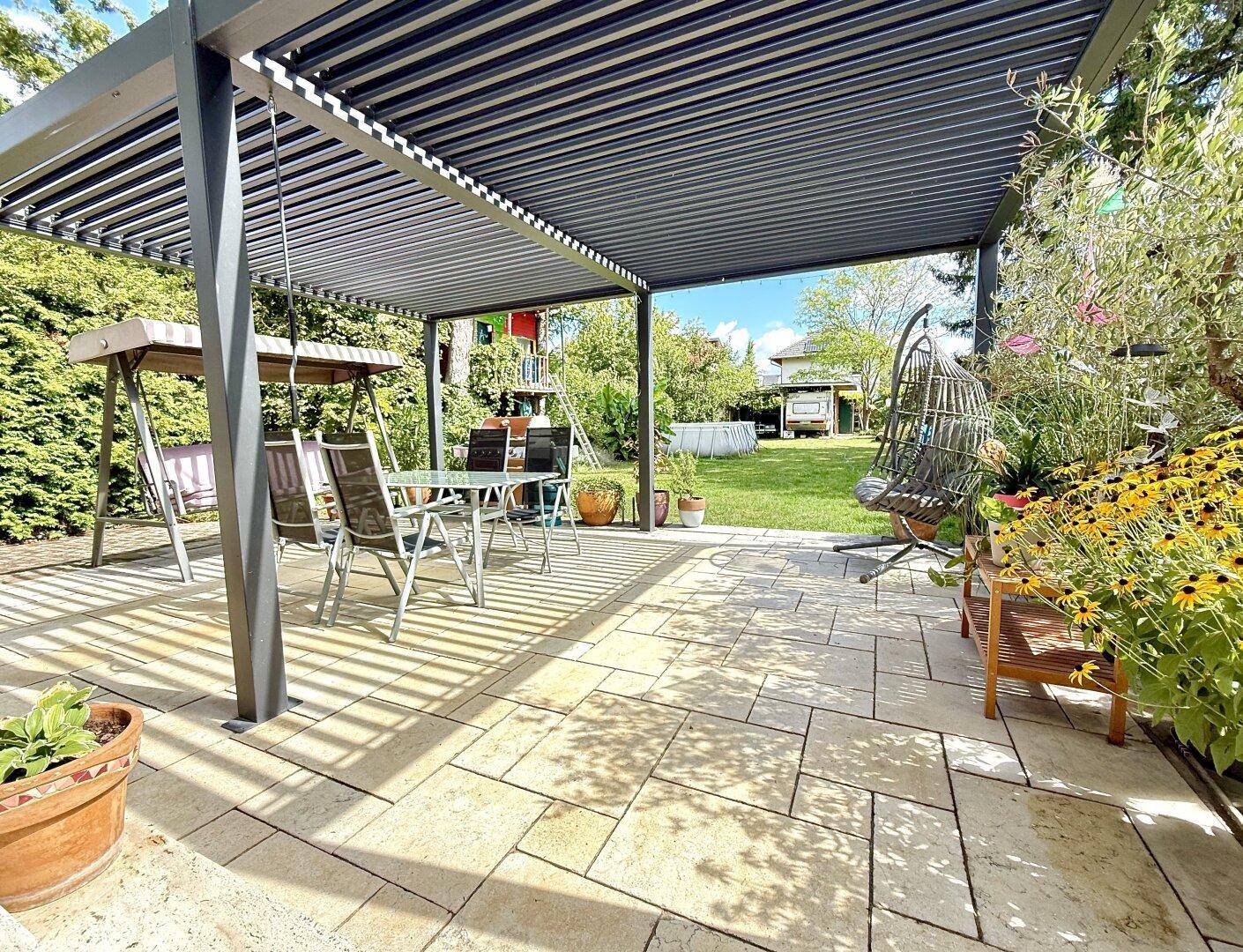 Geräumige, gepflasterte Terrasse unter einer modernen Pergola mit Schaukel und Sitzgelegenheiten.