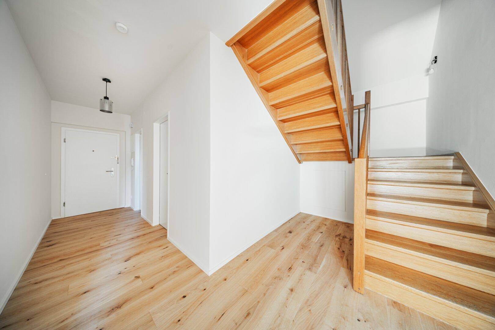Heller Flur mit Holztreppe und Holzboden, der zu den oberen Etagen führt.