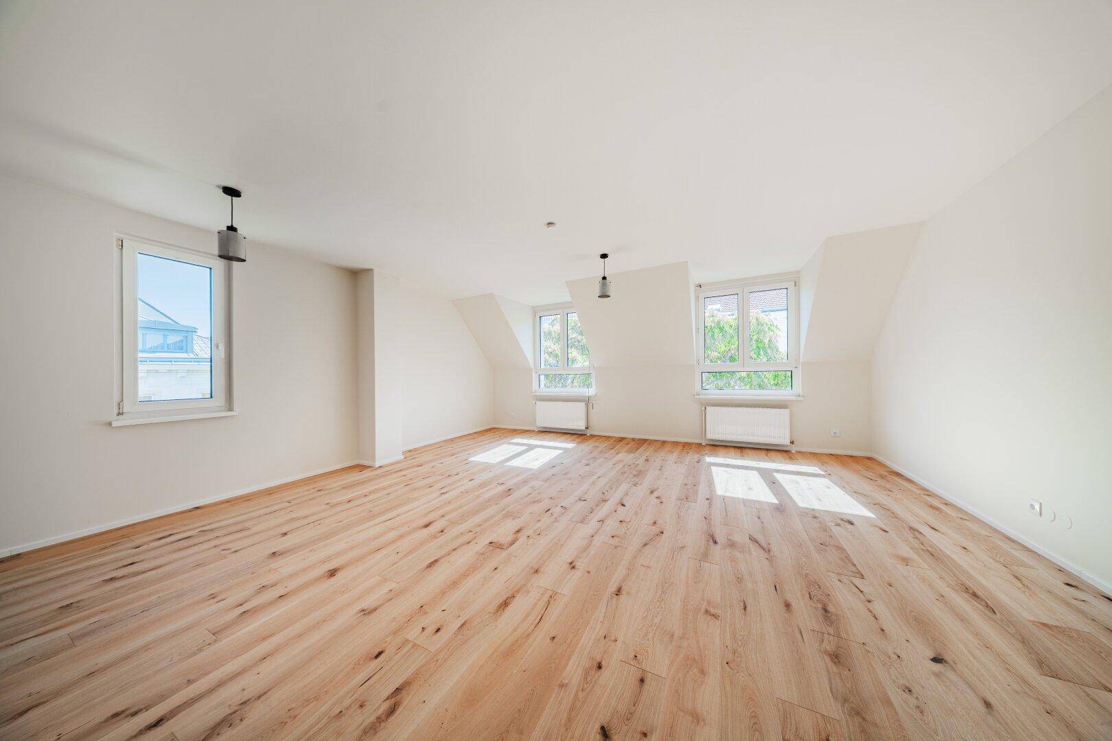 Geräumiges Dachgeschosszimmer mit Holzboden, Dachschrägen und viel Tageslicht durch mehrere Fenster.
