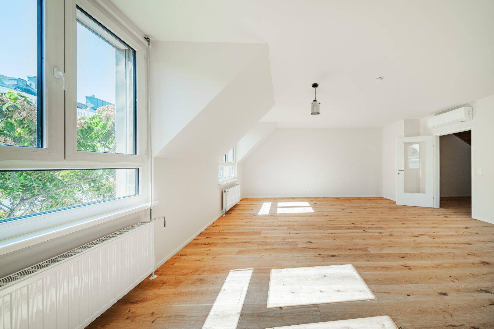 Lichtdurchflutetes Dachgeschosszimmer mit Holzboden, Dachschrägen und Klimaanlage.