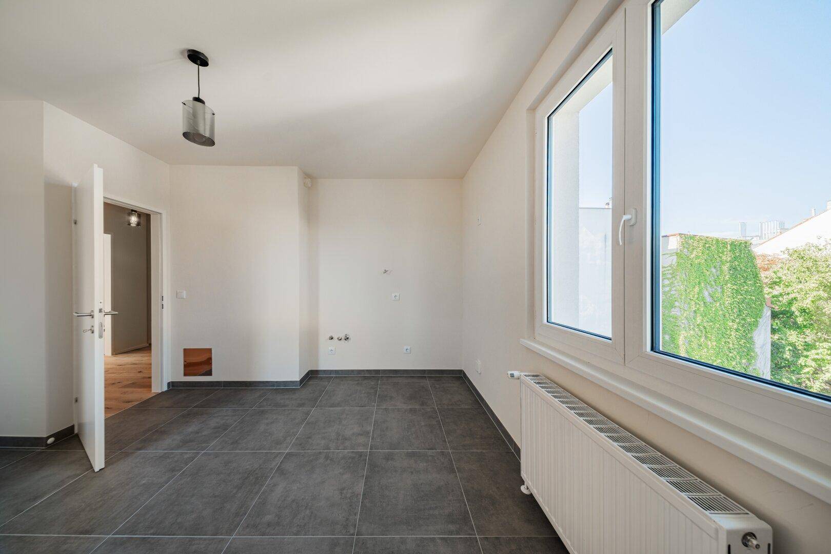 Raum mit grauen Fliesen und Anschlüssen für eine Küche oder Waschküche, mit Fenster.