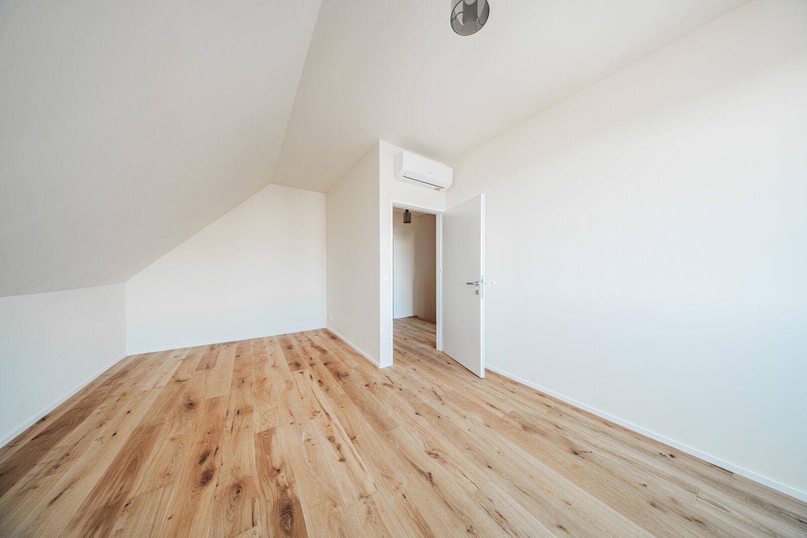 Dachgeschosszimmer mit Holzboden, Dachschräge und Klimaanlage, bereit zur Einrichtung.
