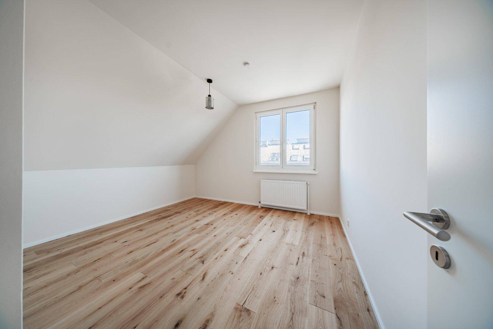 Gemütliches Dachgeschosszimmer mit Holzboden, Dachschräge und Fenster für viel Tageslicht.