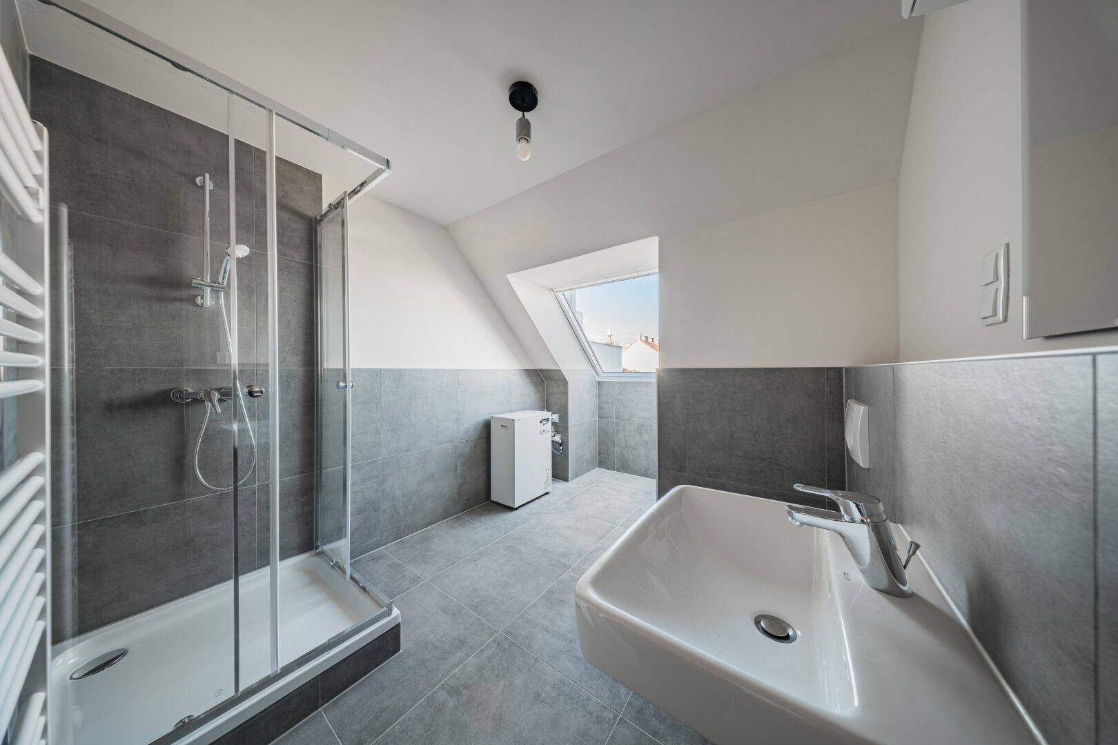 Modernes Badezimmer im Dachgeschoss mit Dusche, Waschbecken und Dachfenster.