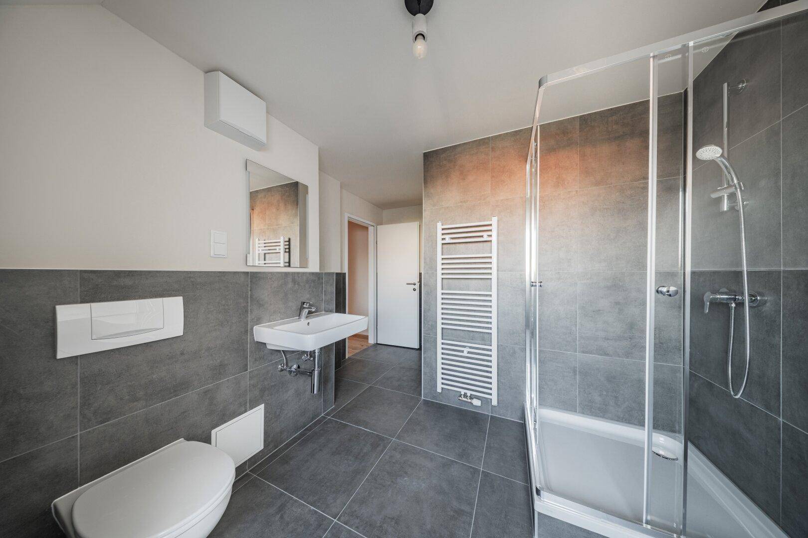 Modernes Badezimmer mit Dusche, Waschbecken, WC und beheiztem Handtuchhalter.