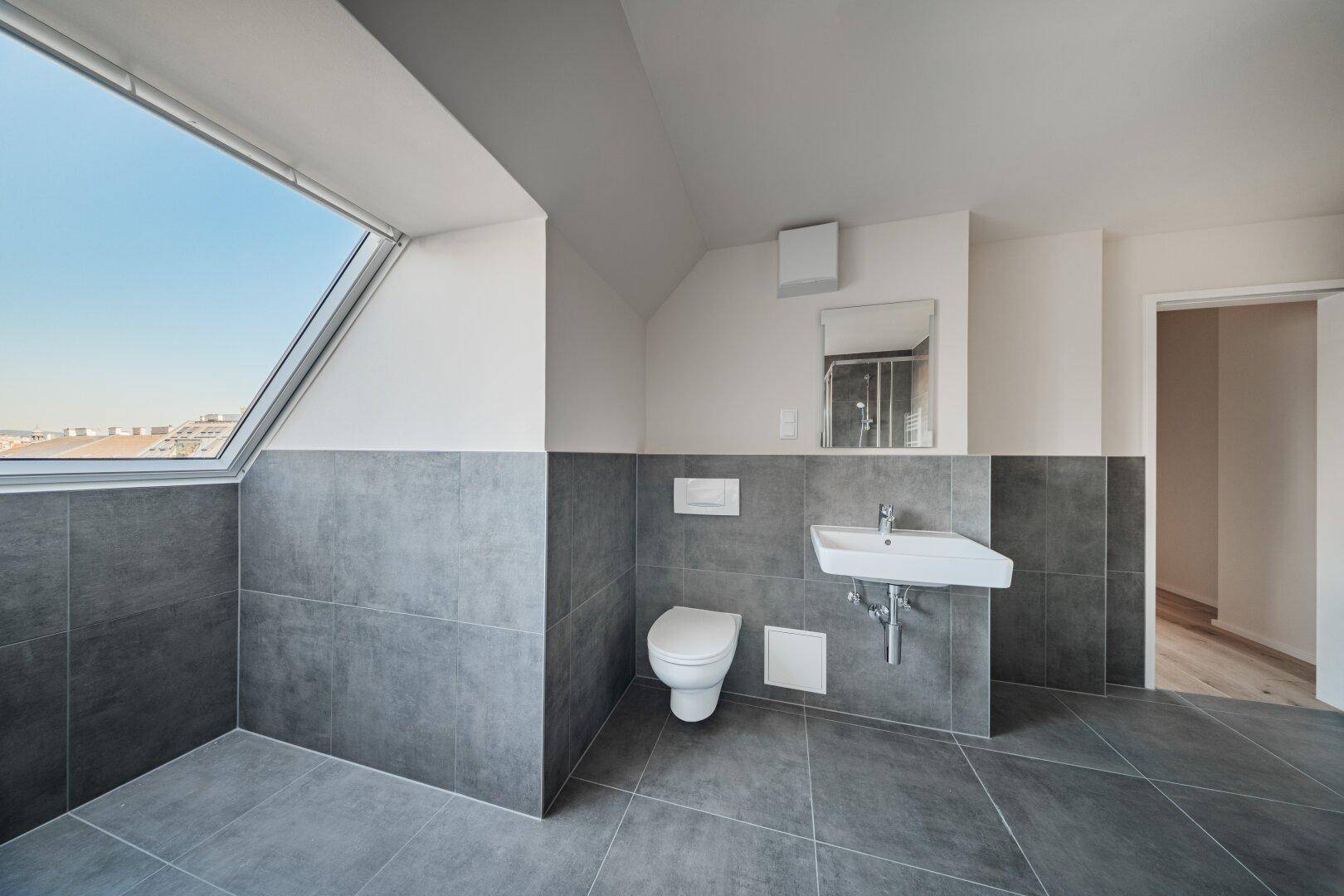Helles Badezimmer im Dachgeschoss mit WC, Waschbecken und großem Dachfenster.