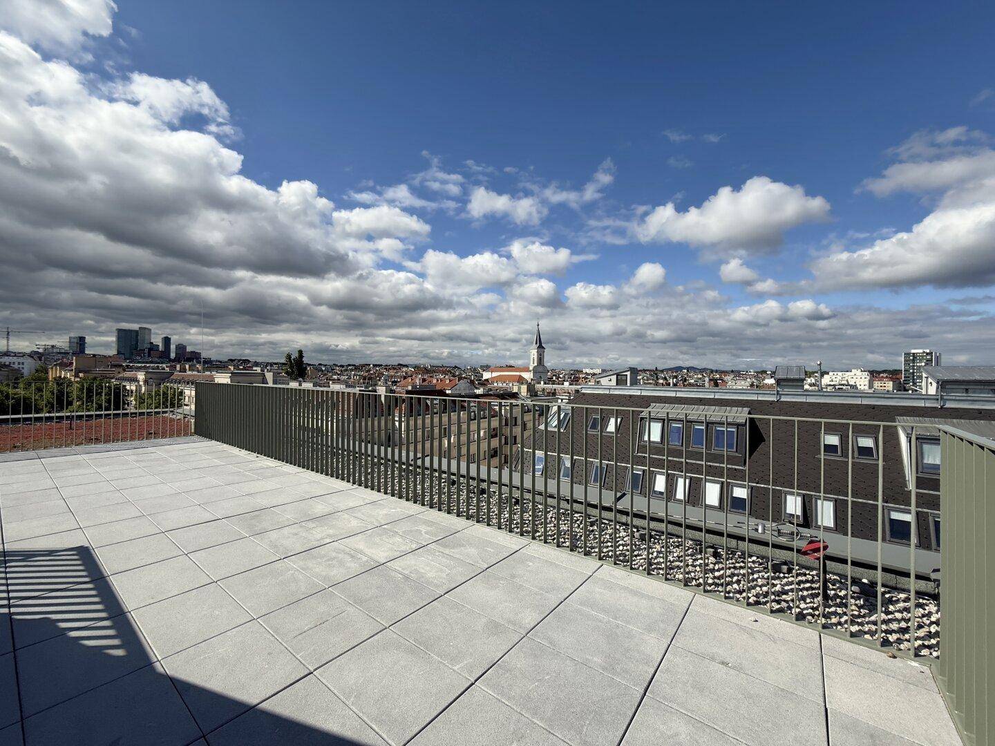 Geräumige Dachterrasse mit weitem Stadtblick und modernem Geländer unter bewölktem Himmel.