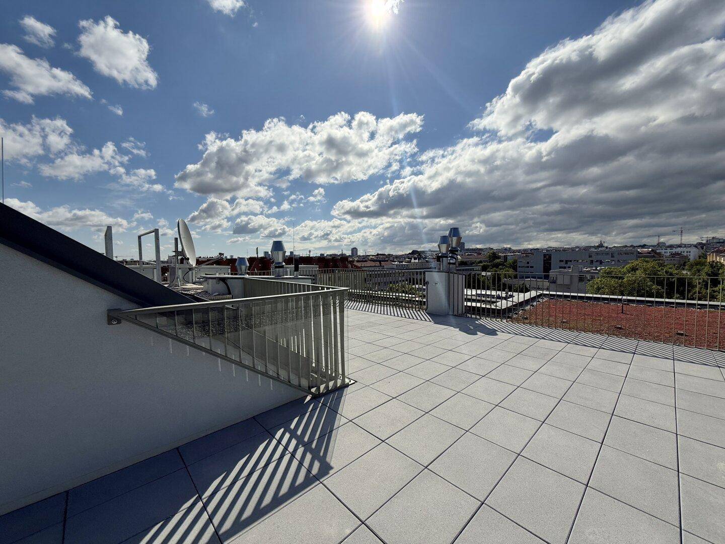Sonnige Dachterrasse mit weitem Stadtblick und moderner Gestaltung unter blauem Himmel.