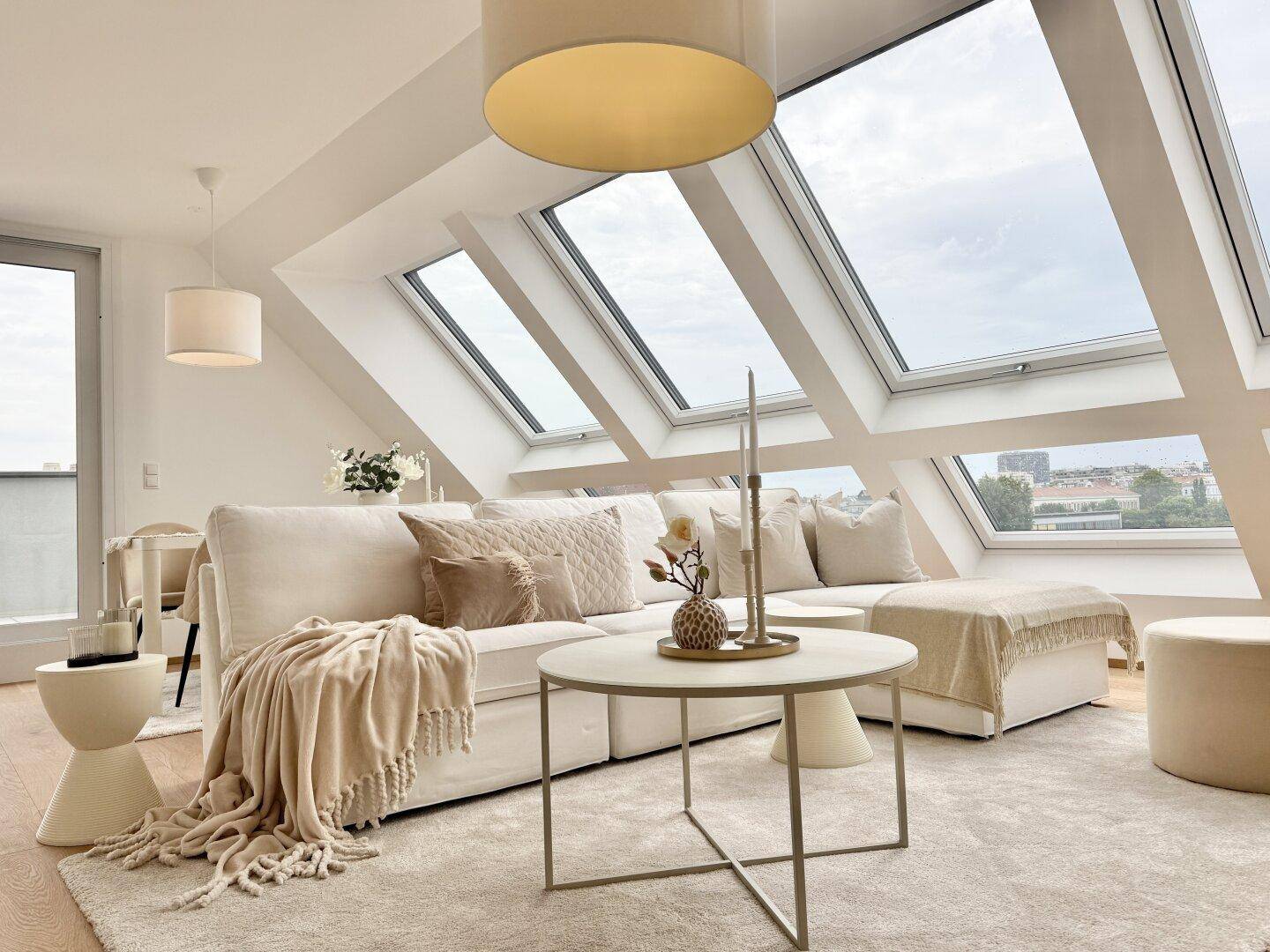 Gemütlicher Wohnbereich mit stilvoller Dekoration, beiger Couch und Blick durch die Dachfenster.