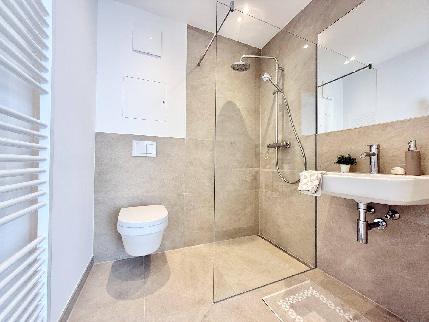 Modernes Badezimmer mit ebenerdiger Dusche, Wand-WC und beigen Fliesen.
