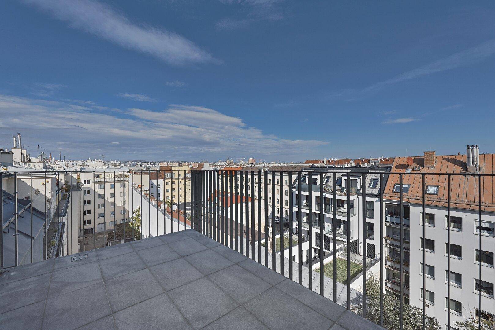 Geräumige Dachterrasse mit Fliesenboden und weitem Blick über die Stadt unter blauem Himmel.