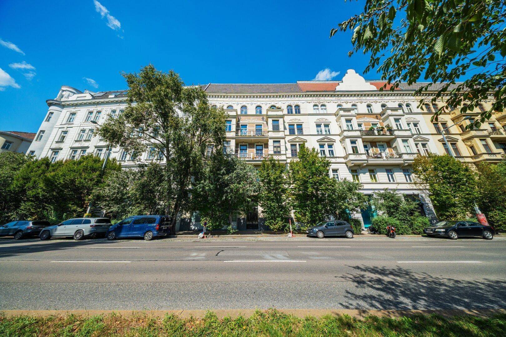 Historisches Mehrfamilienhaus mit vielen Fenstern und Balkonen, gelegen an einer belebten Straße.
