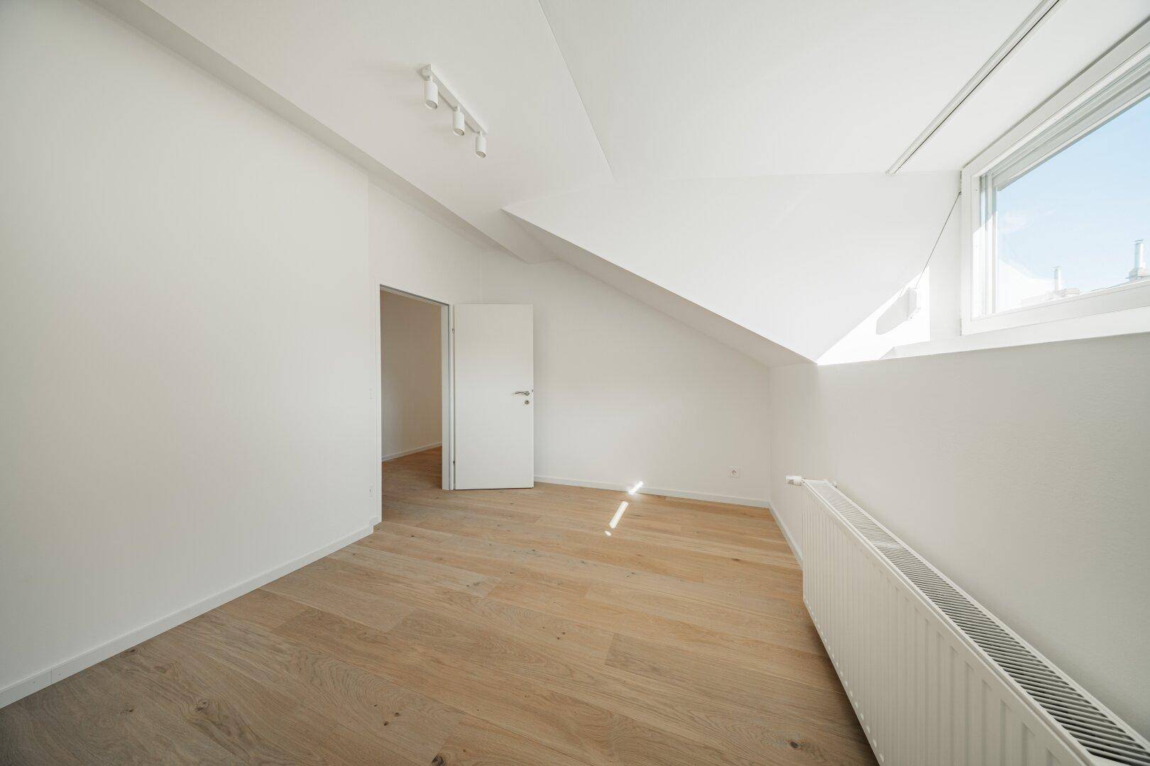 Helles Dachgeschosszimmer mit Holzboden und schrägen Wänden, bereit zur individuellen Gestaltung.