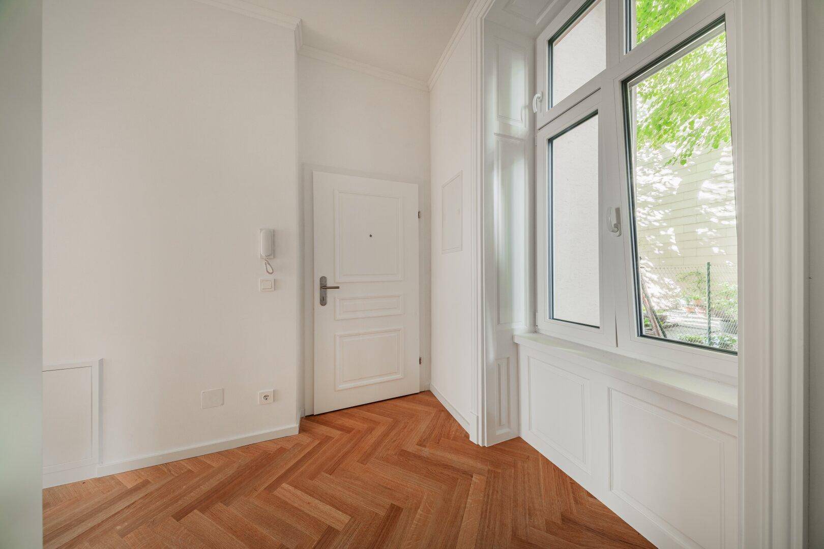 Eingangsbereich mit Fischgrätparkett, Gegensprechanlage und großem Fenster für viel Tageslicht.