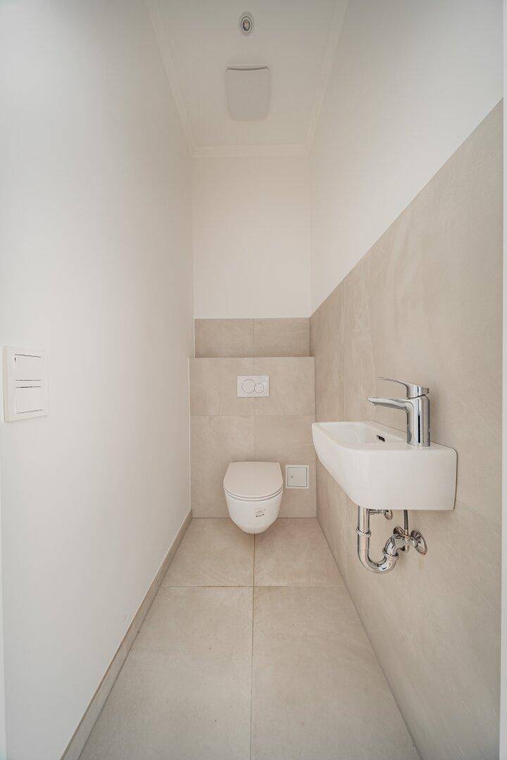Kompaktes Gäste-WC mit wandhängender Toilette und kleinem Waschbecken in modernem Design.