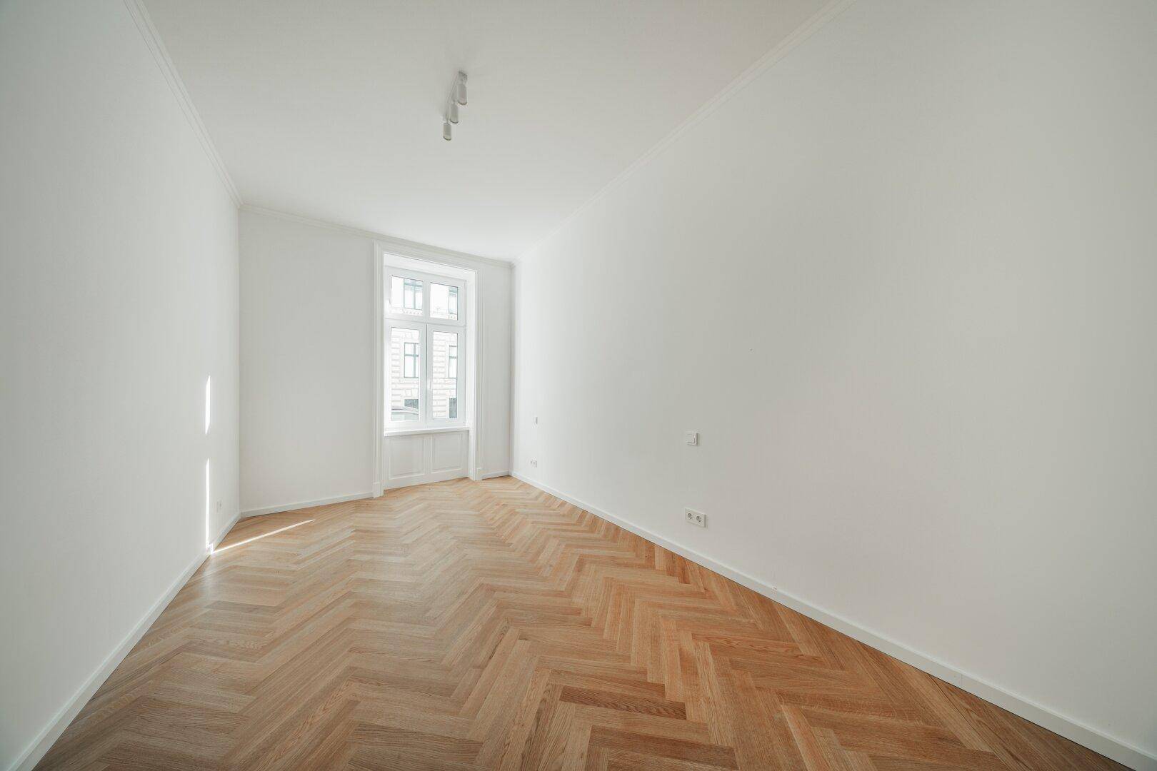 Ruhiges Zimmer mit Fischgrätparkett, weißen Wänden und Blick auf die Stadt.