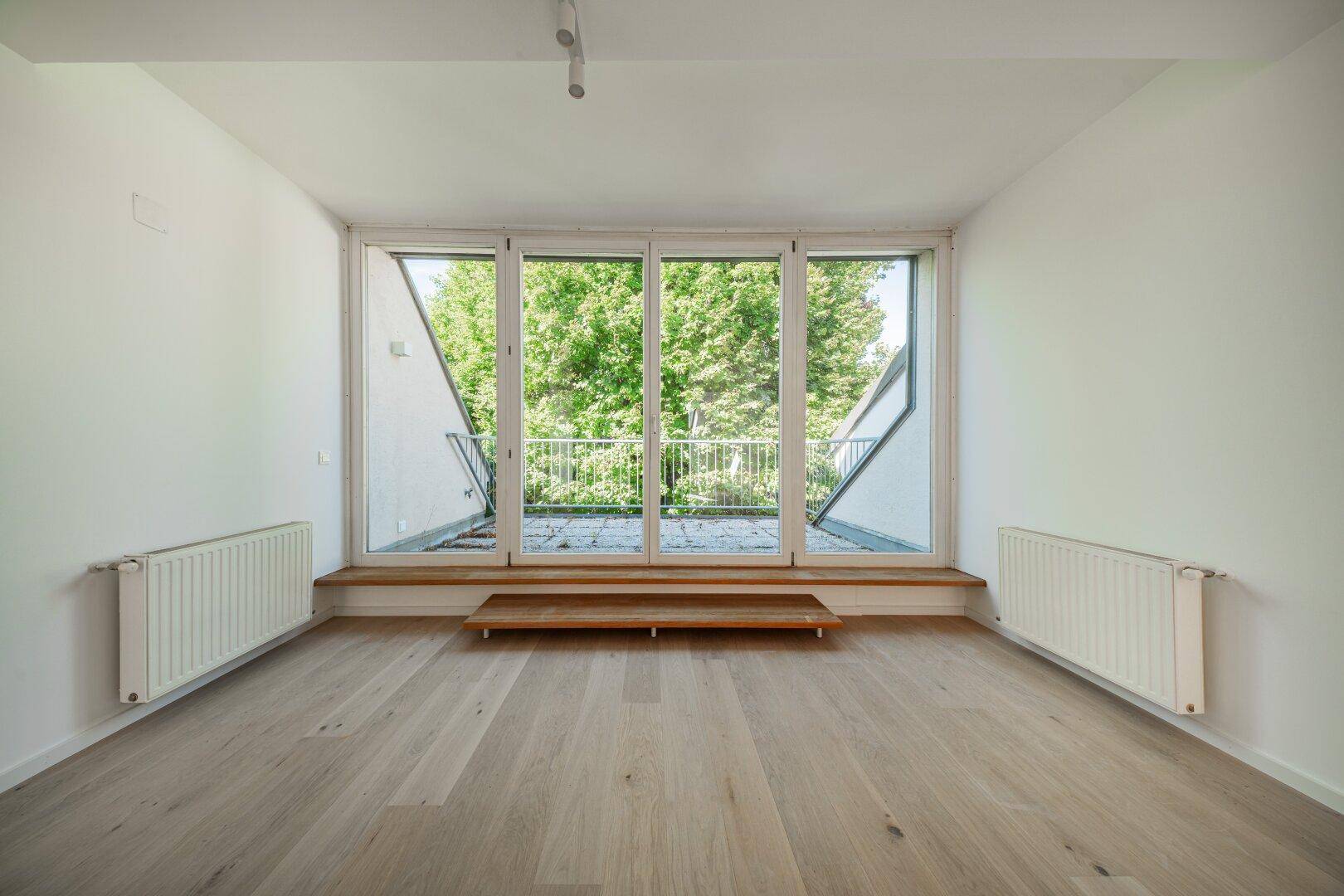 Geräumiger, heller Wohnbereich mit großen Fenstern und Blick ins Grüne, ausgestattet mit Heizkörpern.