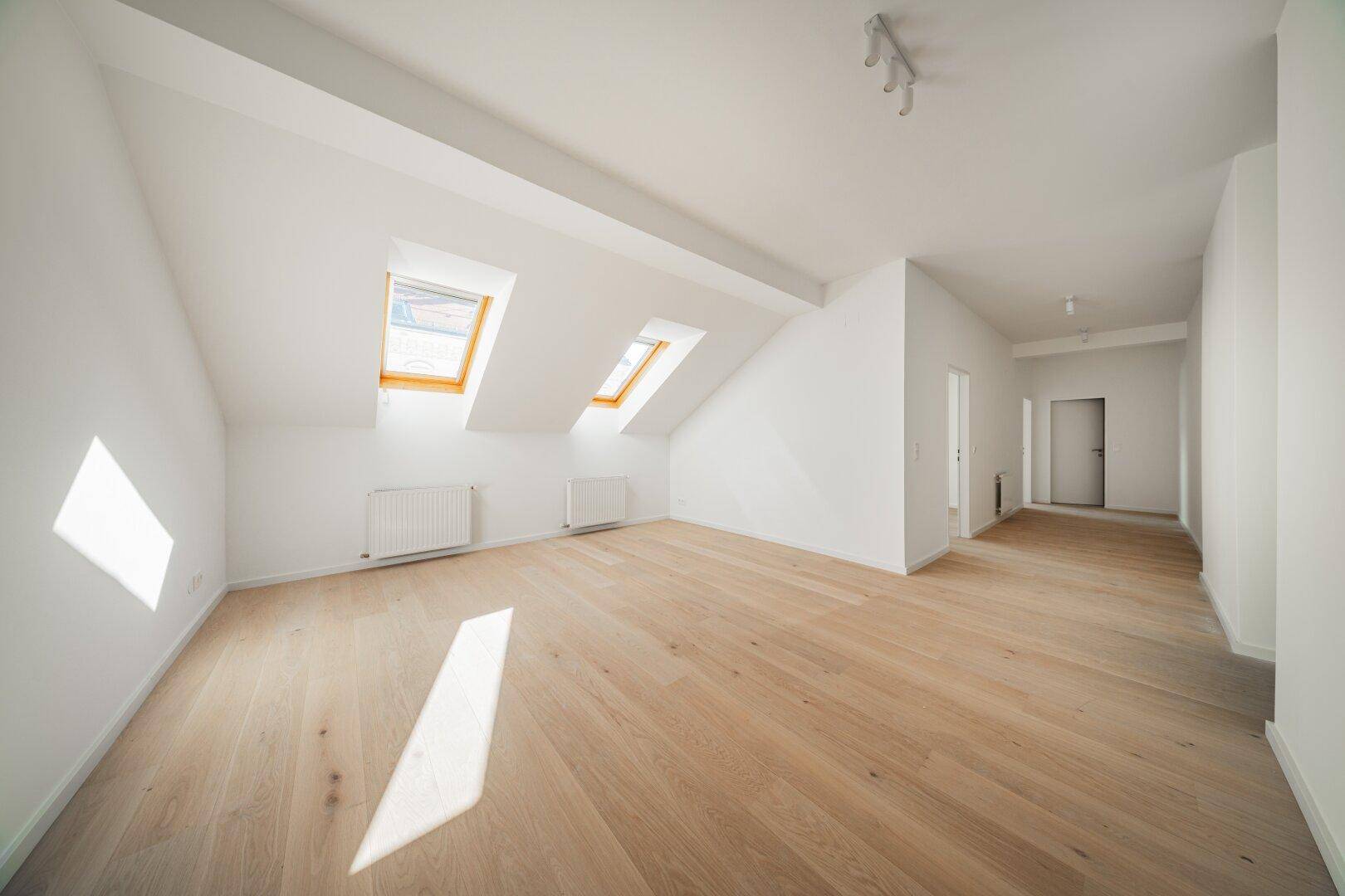 Heller Dachgeschossraum mit Holzboden und Dachfenstern, die viel natürliches Licht hereinlassen.