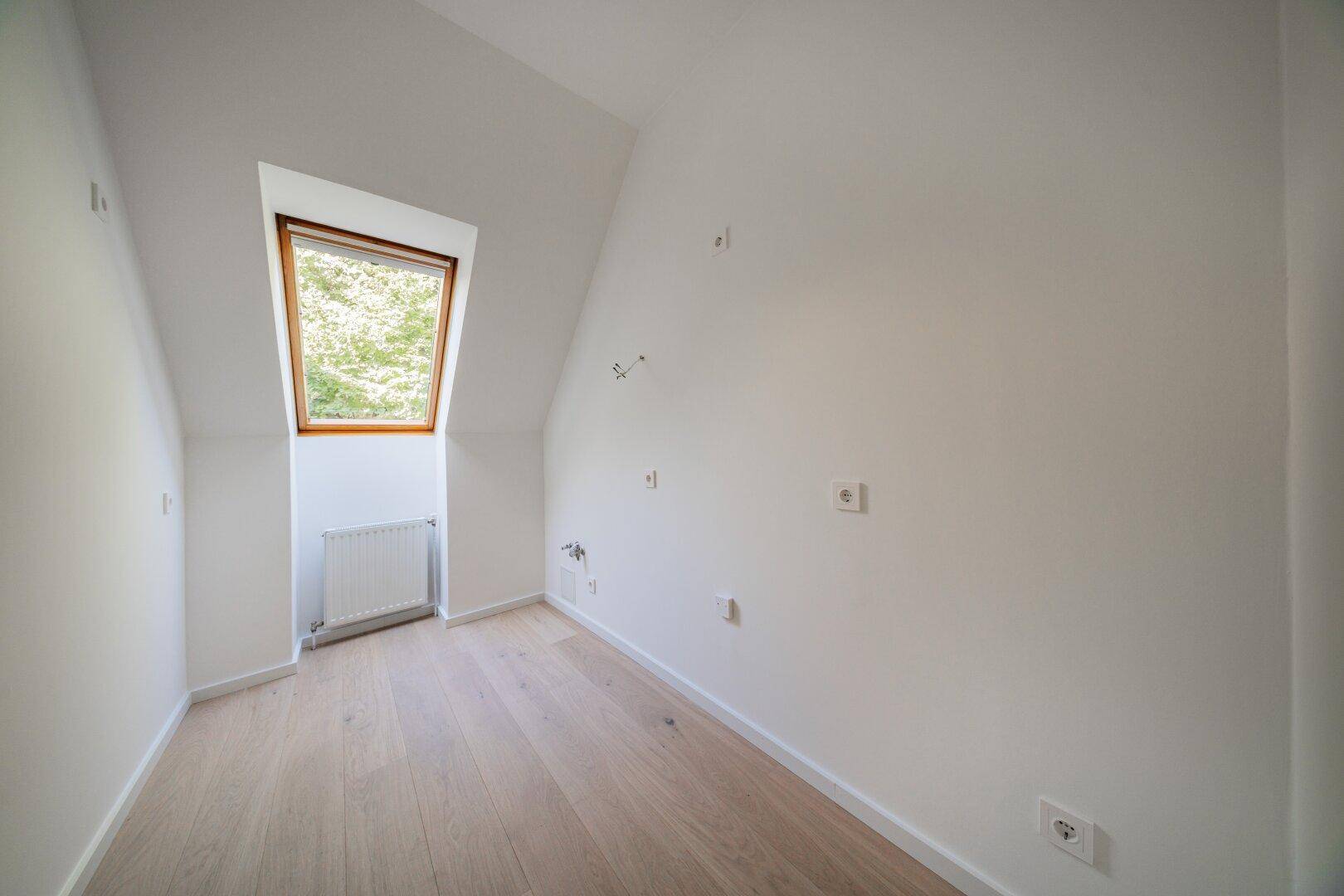 Kleinerer Dachgeschossraum mit Holzboden und einem Dachfenster, das viel Licht spendet.