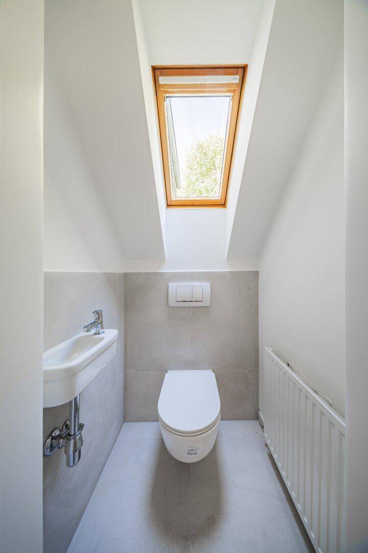 Modernes Gäste-WC mit wandhängender Toilette, kleinem Waschbecken und Dachfenster.