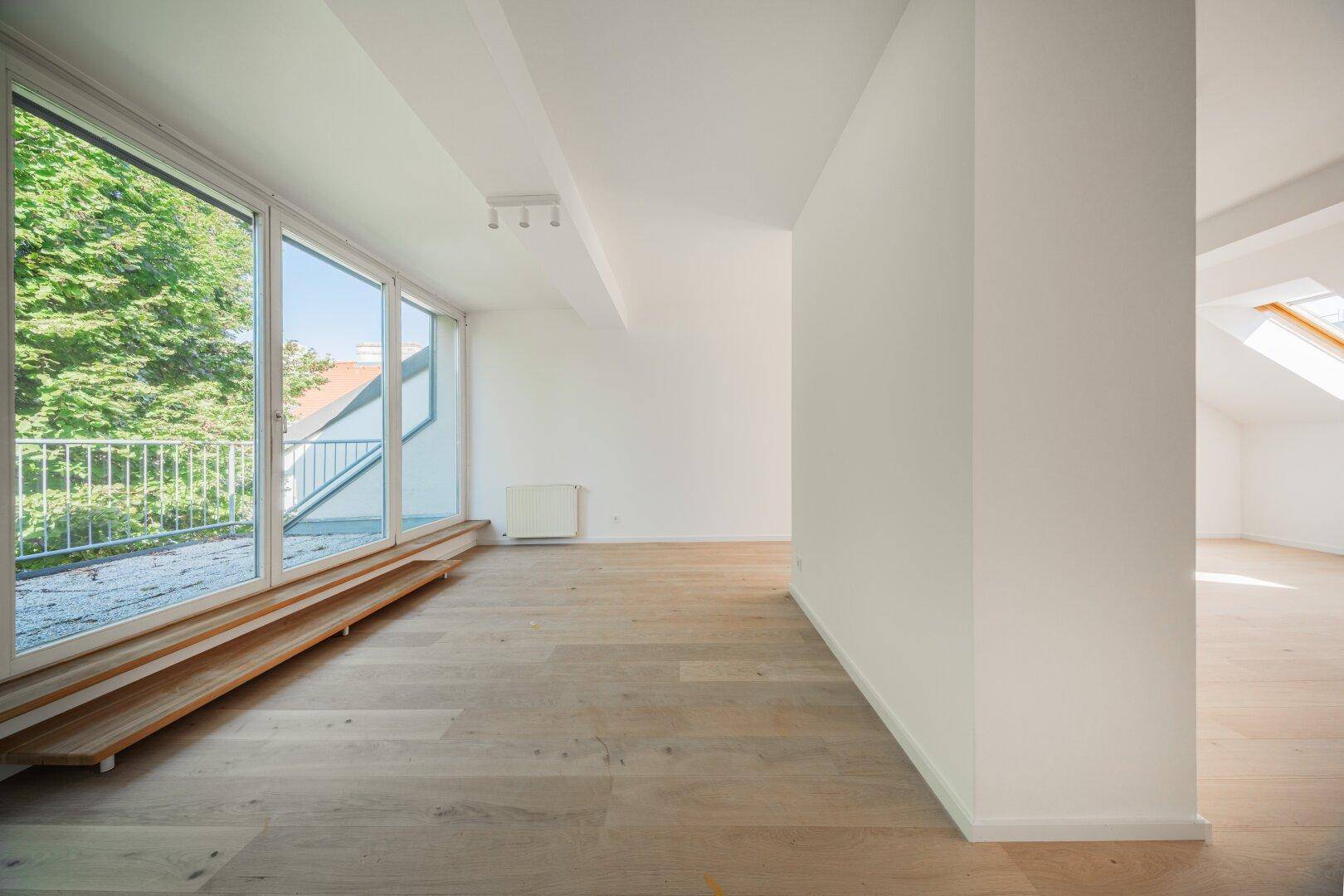 Lichtdurchfluteter Wohnraum mit Holzboden und breiter Fensterfront, die einen Blick ins Grüne bietet.