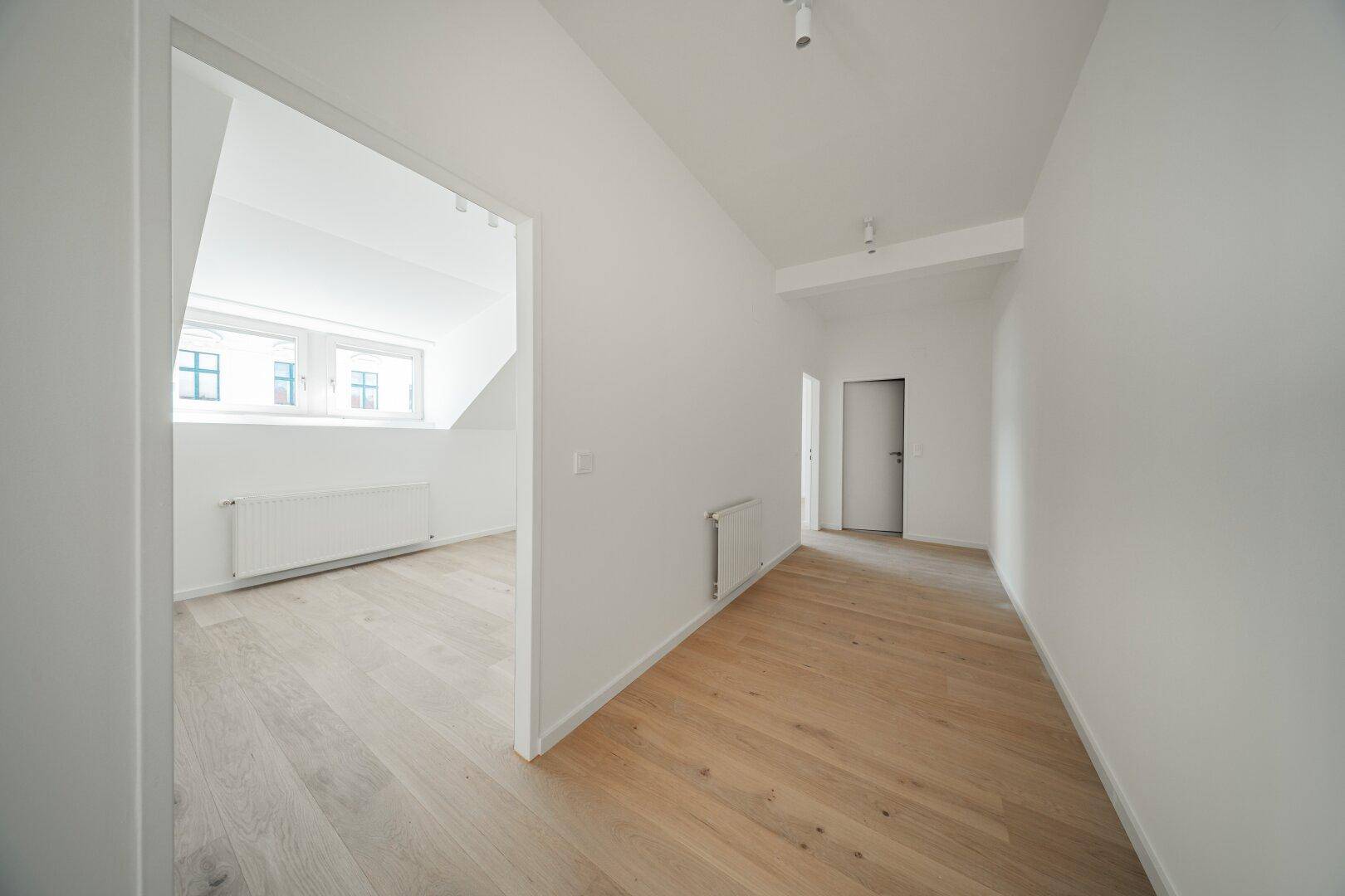 Langer, heller Flur mit Holzboden, der zu weiteren Zimmern und einem Dachgeschossraum führt.