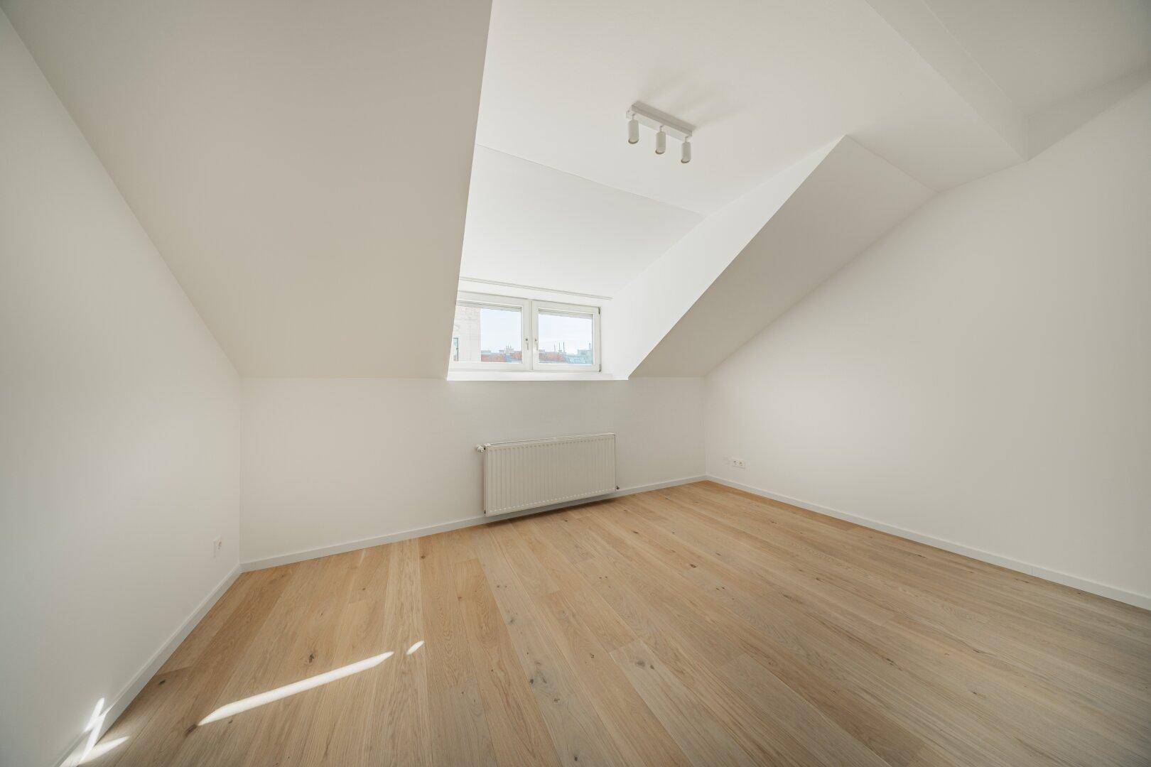 Geräumiges Dachgeschosszimmer mit Holzboden und einem Fenster, das den Raum hell erscheinen lässt.