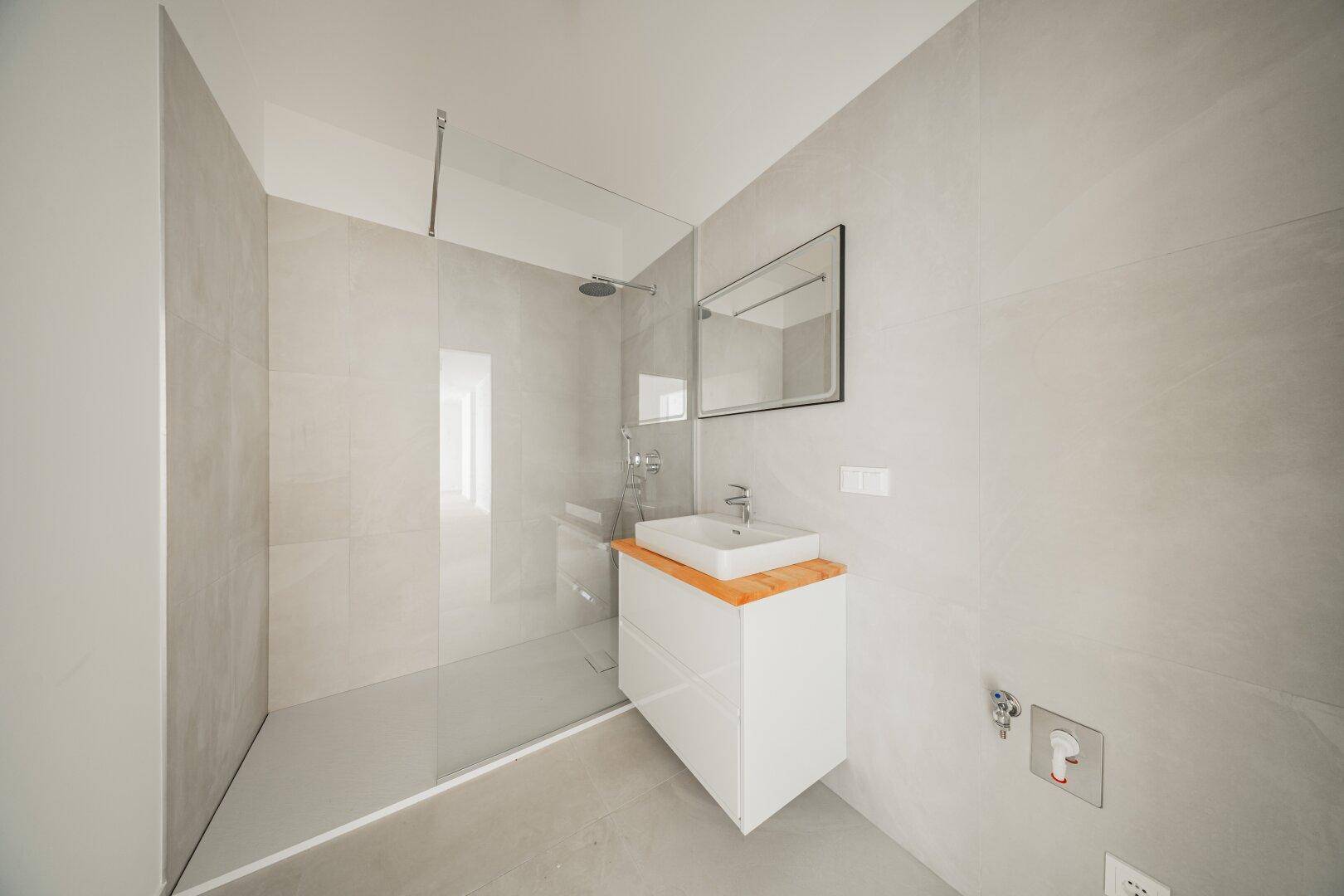 Modernes Badezimmer mit begehbarer Dusche, minimalistischem Waschbecken und grauen Fliesen.