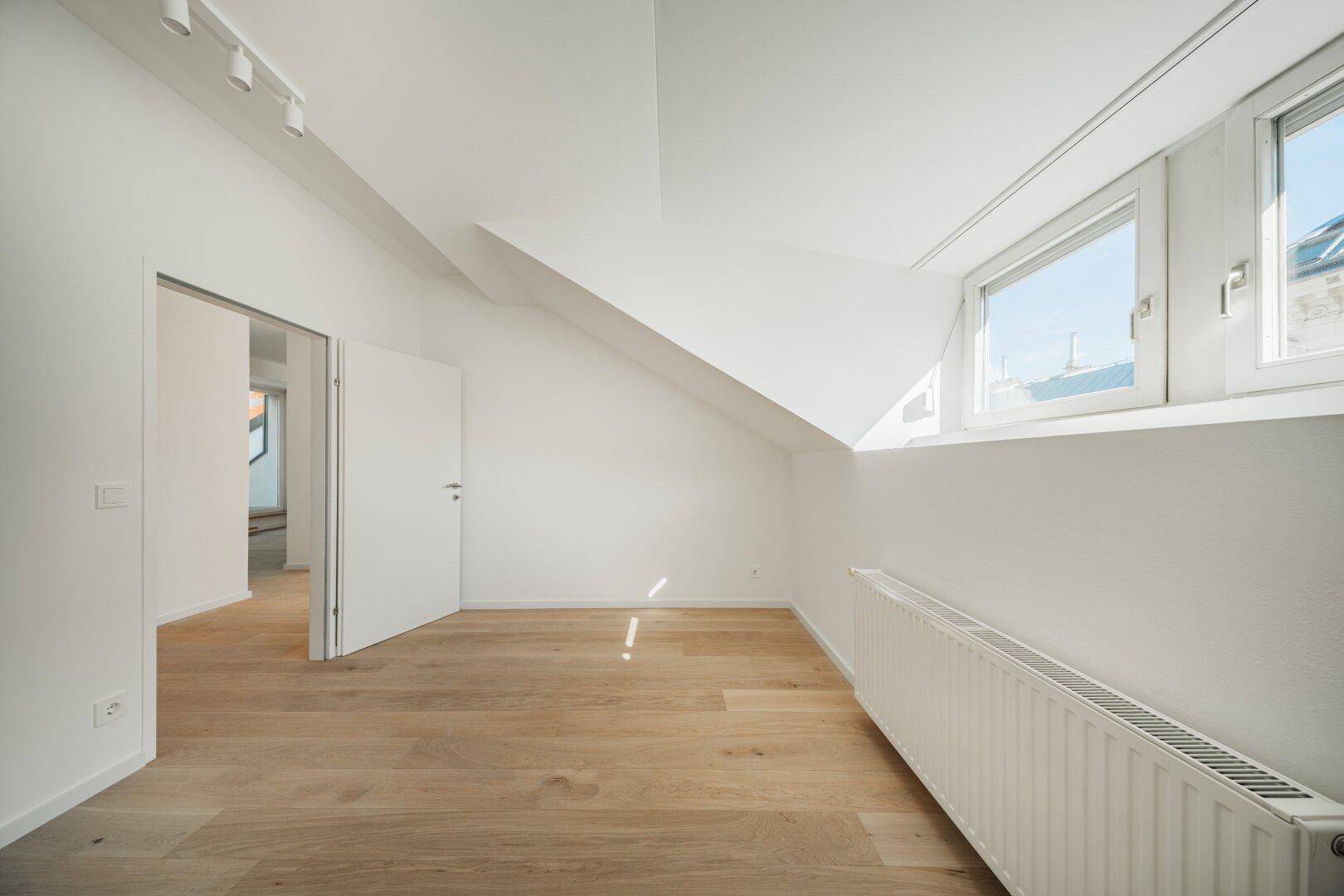 Helles Zimmer im Dachgeschoss mit Holzboden und schrägen Wänden, ideal als Schlaf- oder Arbeitszimmer.