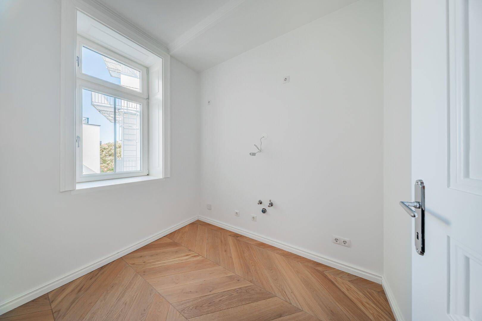 Kleiner Raum mit Fischgrätparkett und Fenster, vorbereitet für Installationen mit sichtbaren Anschlüssen.