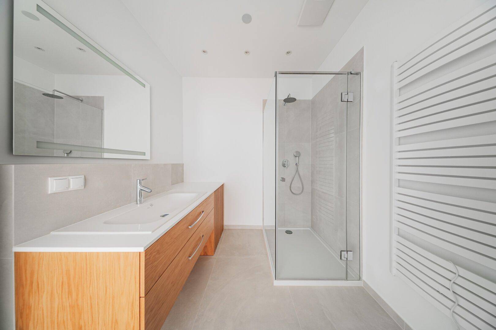 Modernes Badezimmer mit Doppelwaschbecken, begehbarer Dusche und beheiztem Handtuchhalter.