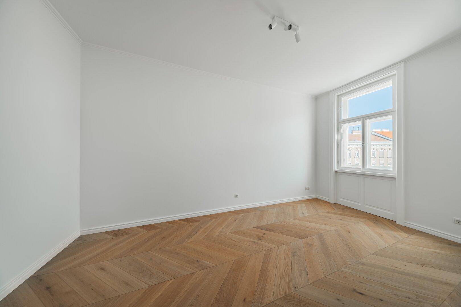 Lichtdurchfluteter Raum mit elegantem Fischgrätparkett und Blick auf die Stadt durch große Fenster.