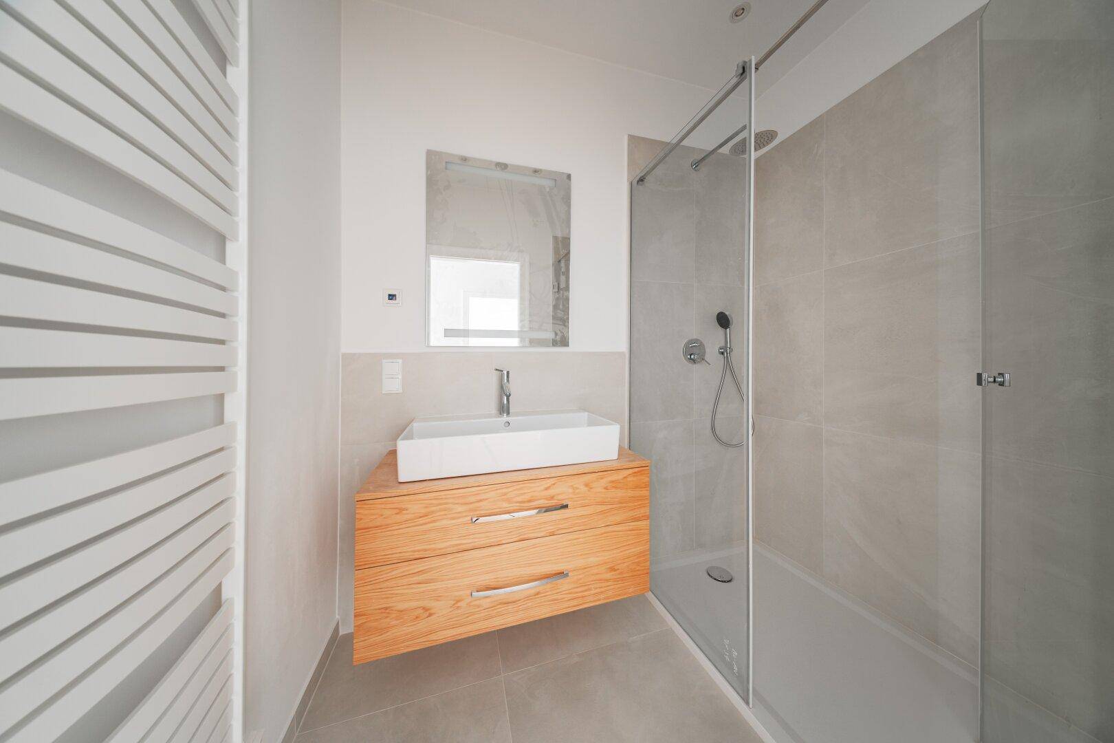 Modernes Badezimmer mit begehbarer Dusche, Holzwaschtisch und beheiztem Handtuchhalter.