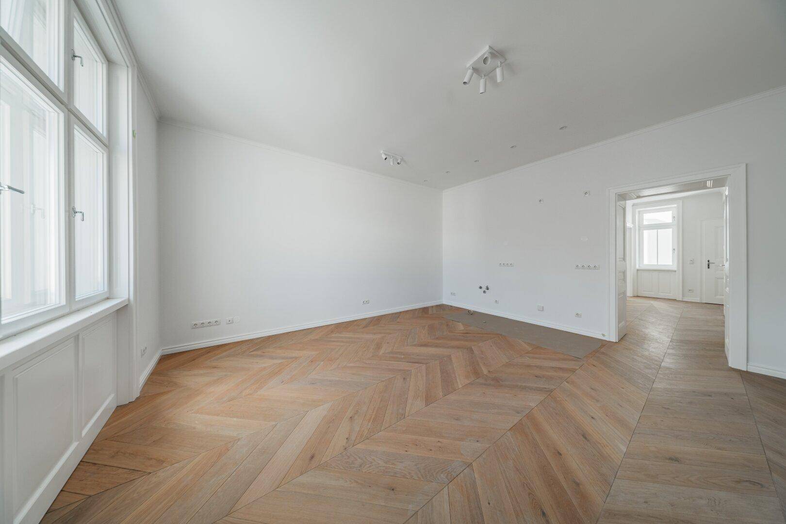 Geräumiges, helles Zimmer mit elegantem Fischgrätparkett und großen Fenstern.