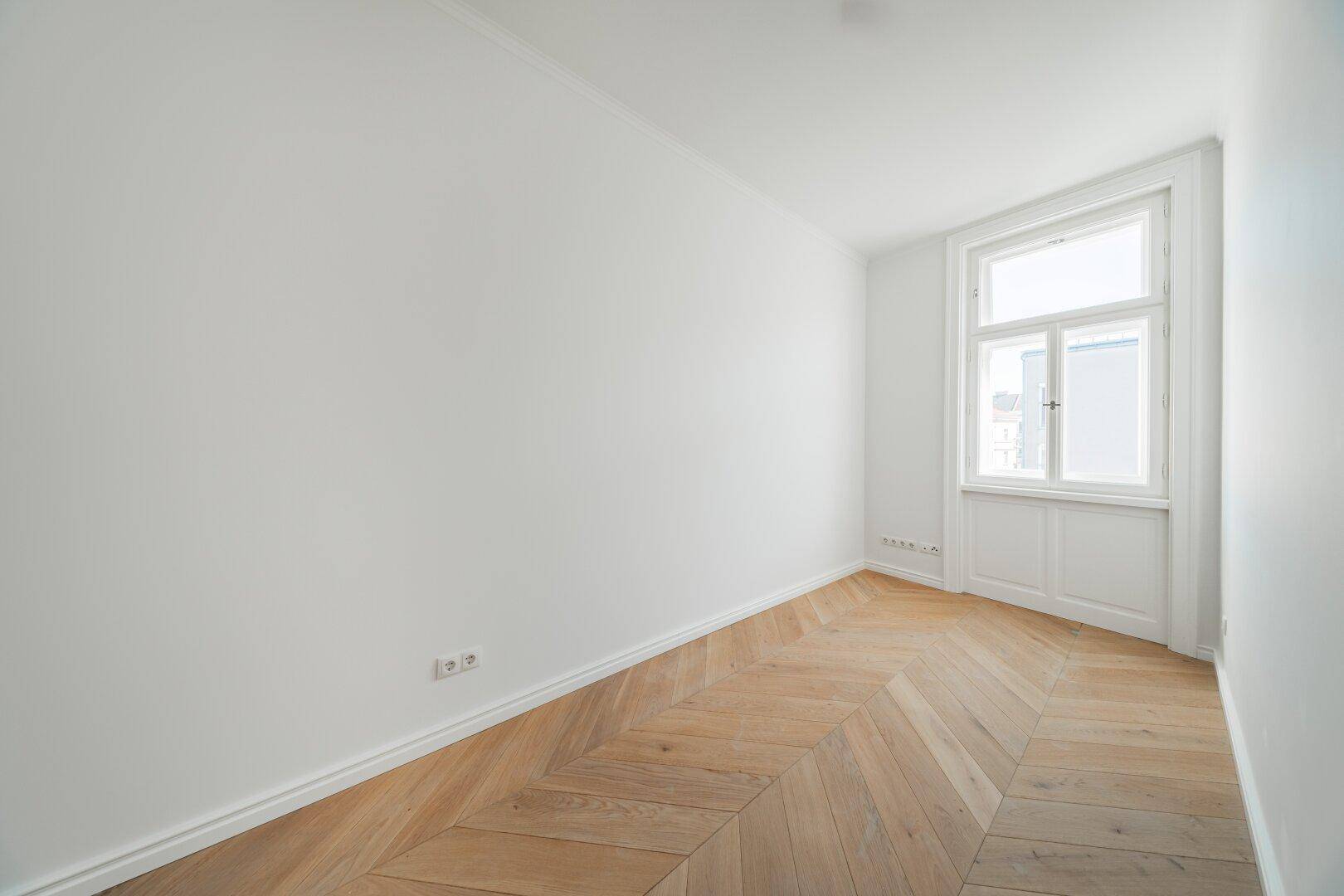 Ruhiges Zimmer mit Fischgrätparkett und einem Fenster, ideal als Schlaf- oder Arbeitszimmer.
