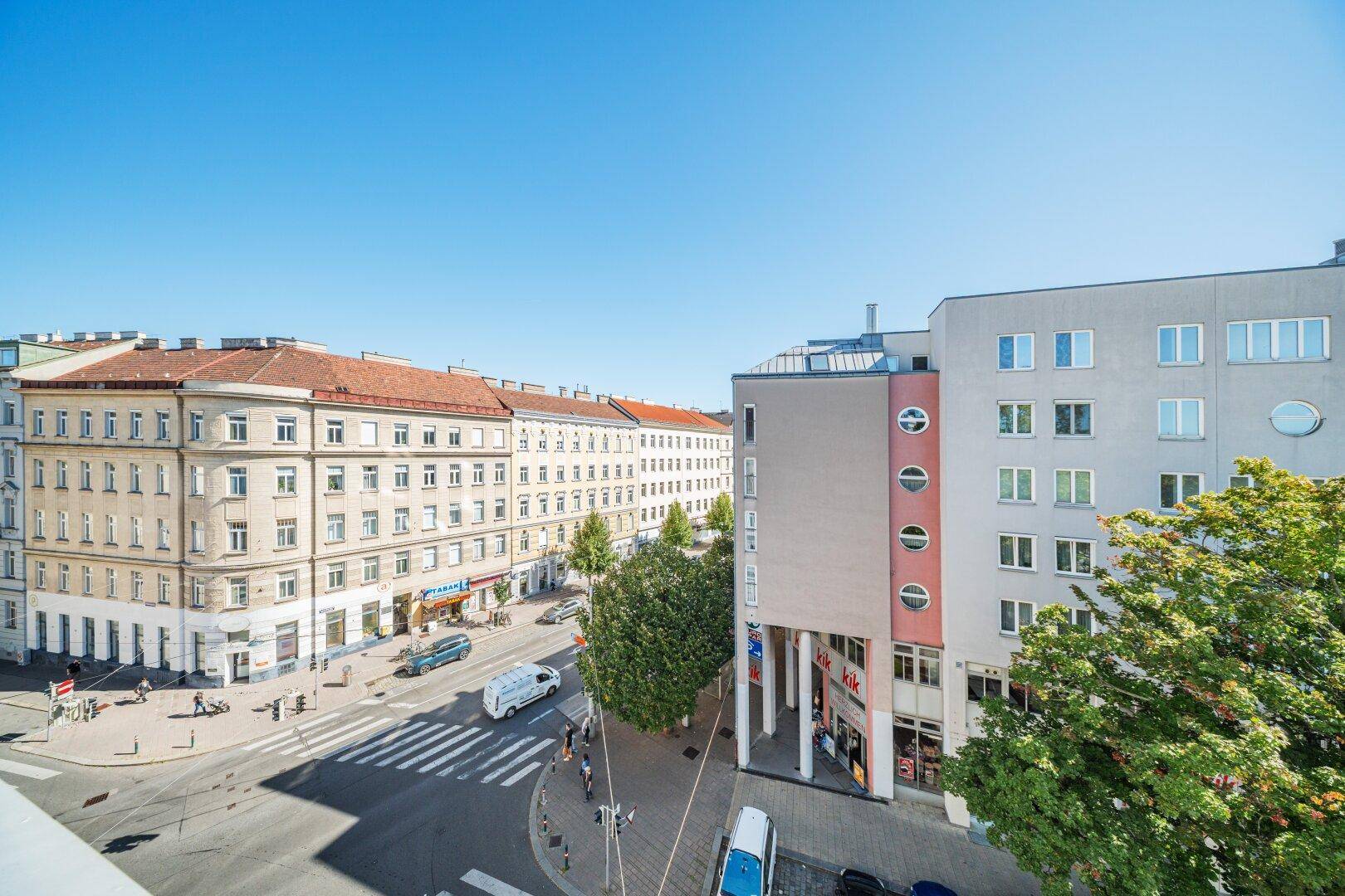 Weitblick über eine belebte Stadtstraße mit historischen und modernen Gebäuden unter blauem Himmel.