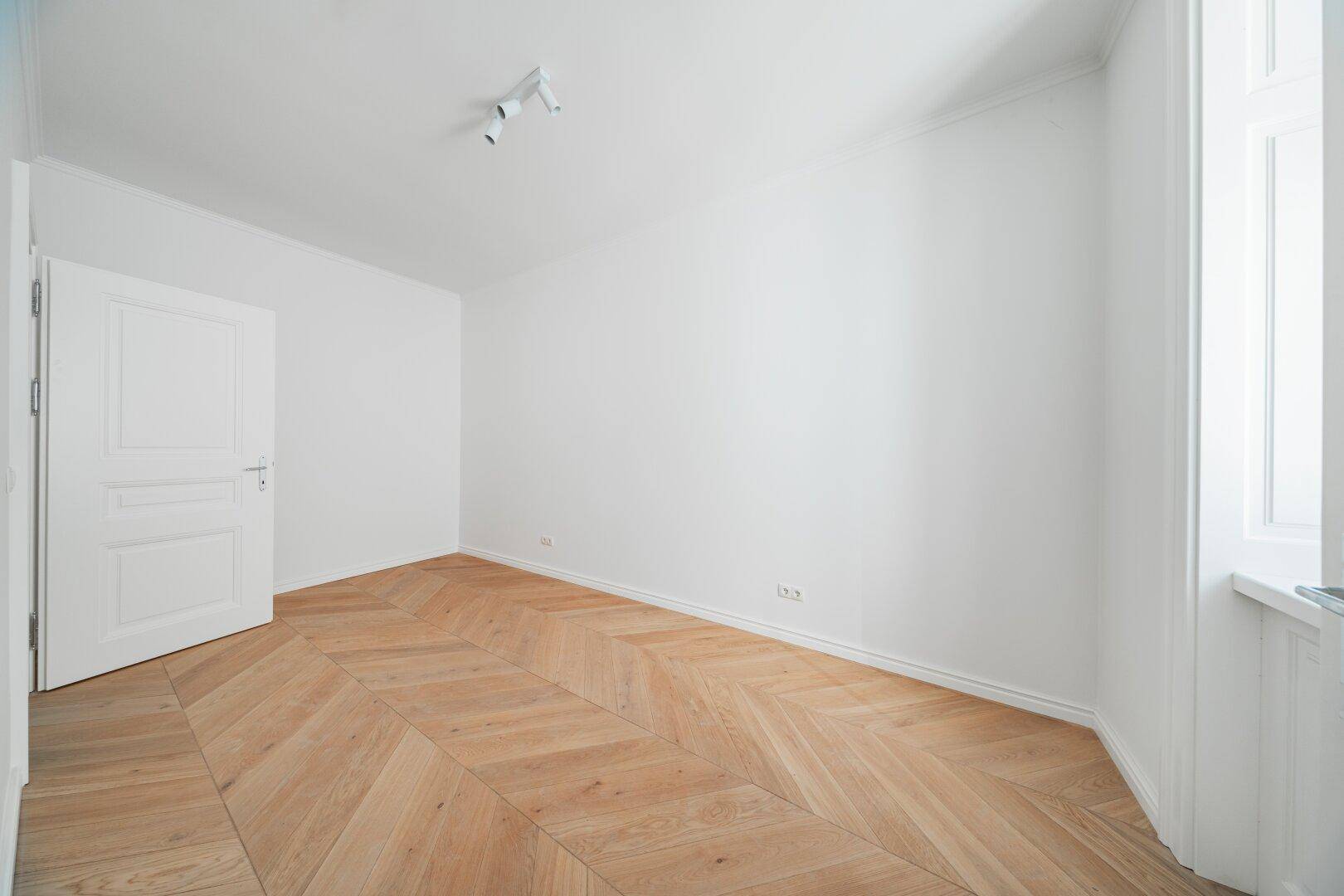 Leeres, helles Zimmer mit Fischgrätparkett und weißer Tür, bereit für neue Bewohner.