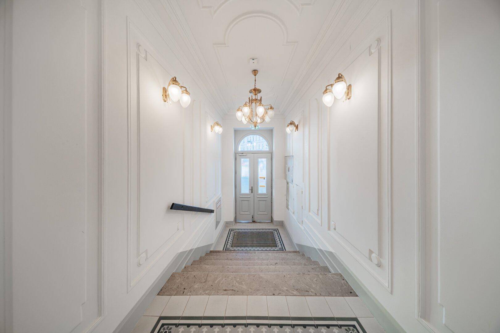 Eleganter Eingangsbereich mit breiter Steintreppe, kunstvollem Geländer und dekorativem Fliesenboden.