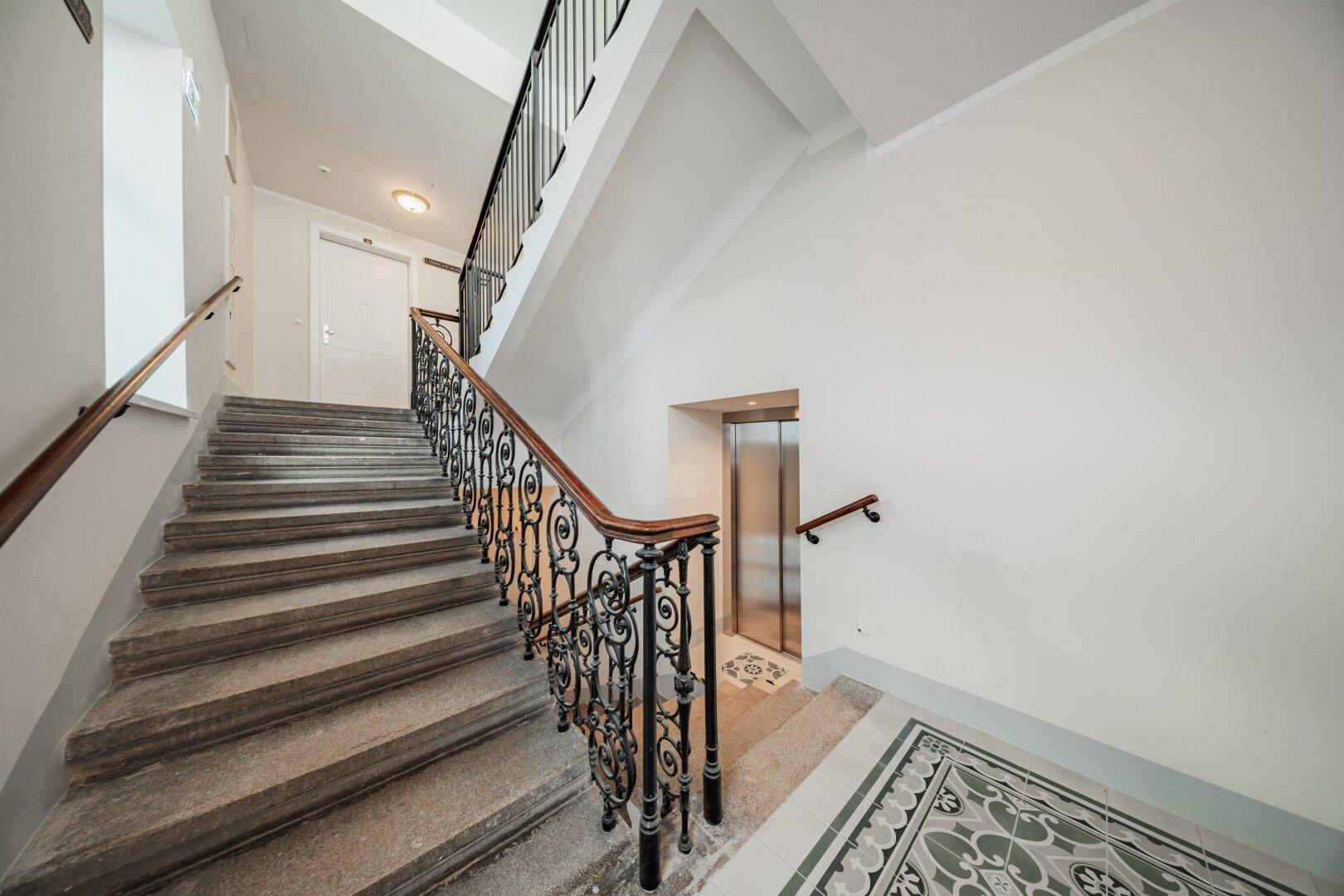 Geräumiges Treppenhaus mit Steinstufen, kunstvollem Geländer und integriertem modernen Aufzug.