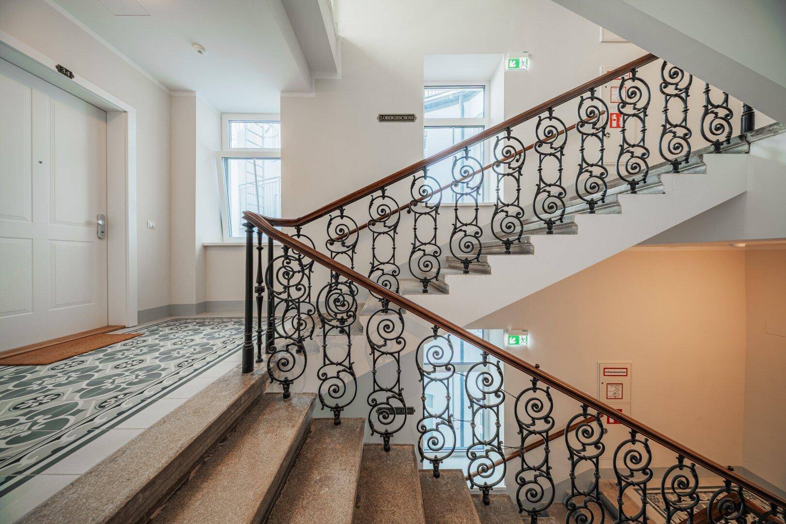 Elegantes Treppenhaus mit detailreichem schmiedeeisernem Geländer und hellen Fenstern.
