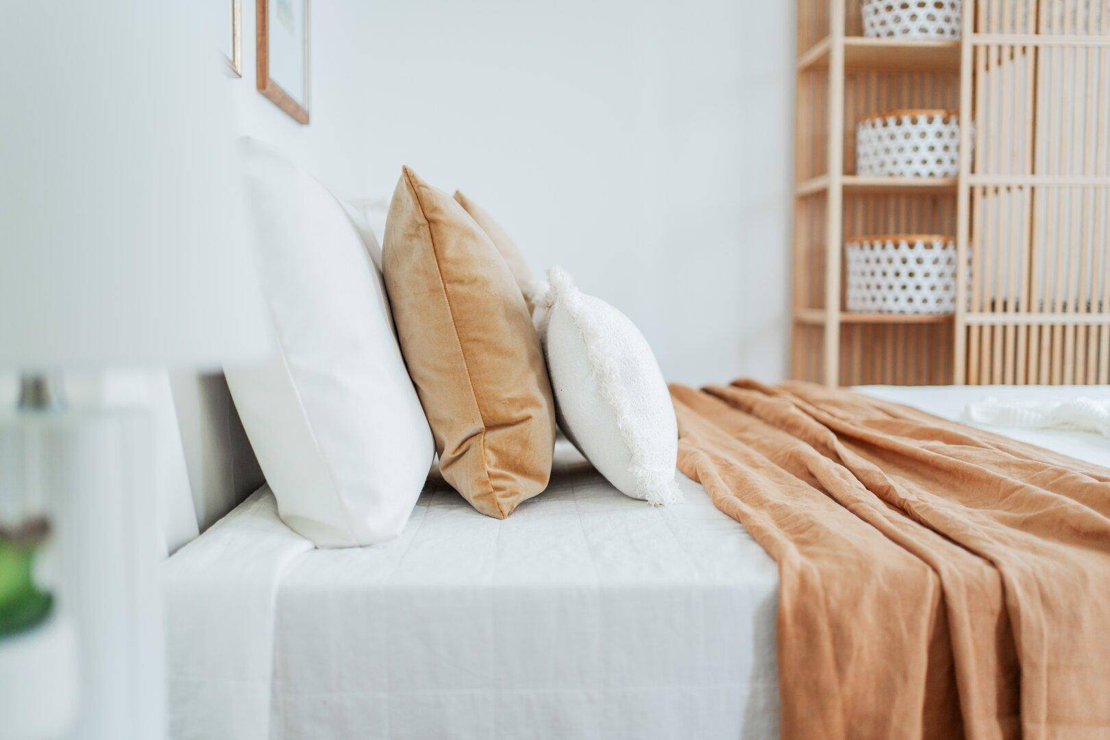 Detailaufnahme eines Bettes mit beigen Kissen und Decke in einem hellen Schlafzimmer.
