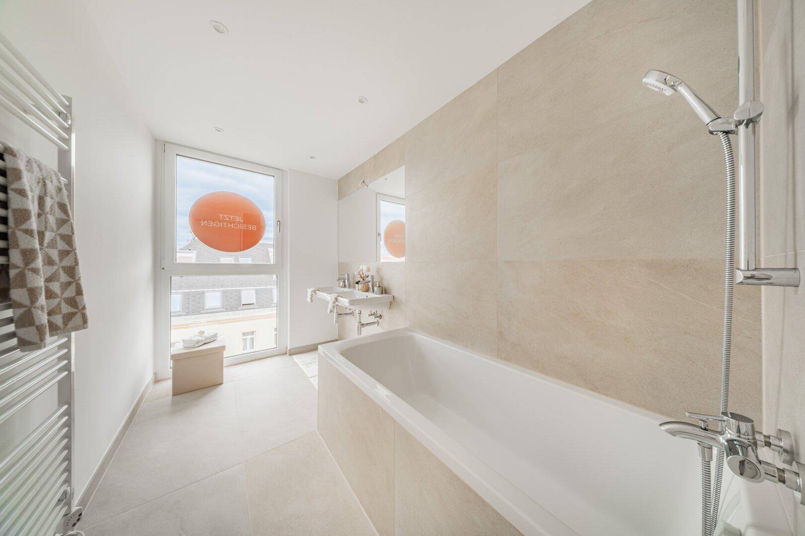 Modernes Badezimmer mit Badewanne, beigen Fliesen und Fenster für Tageslicht.