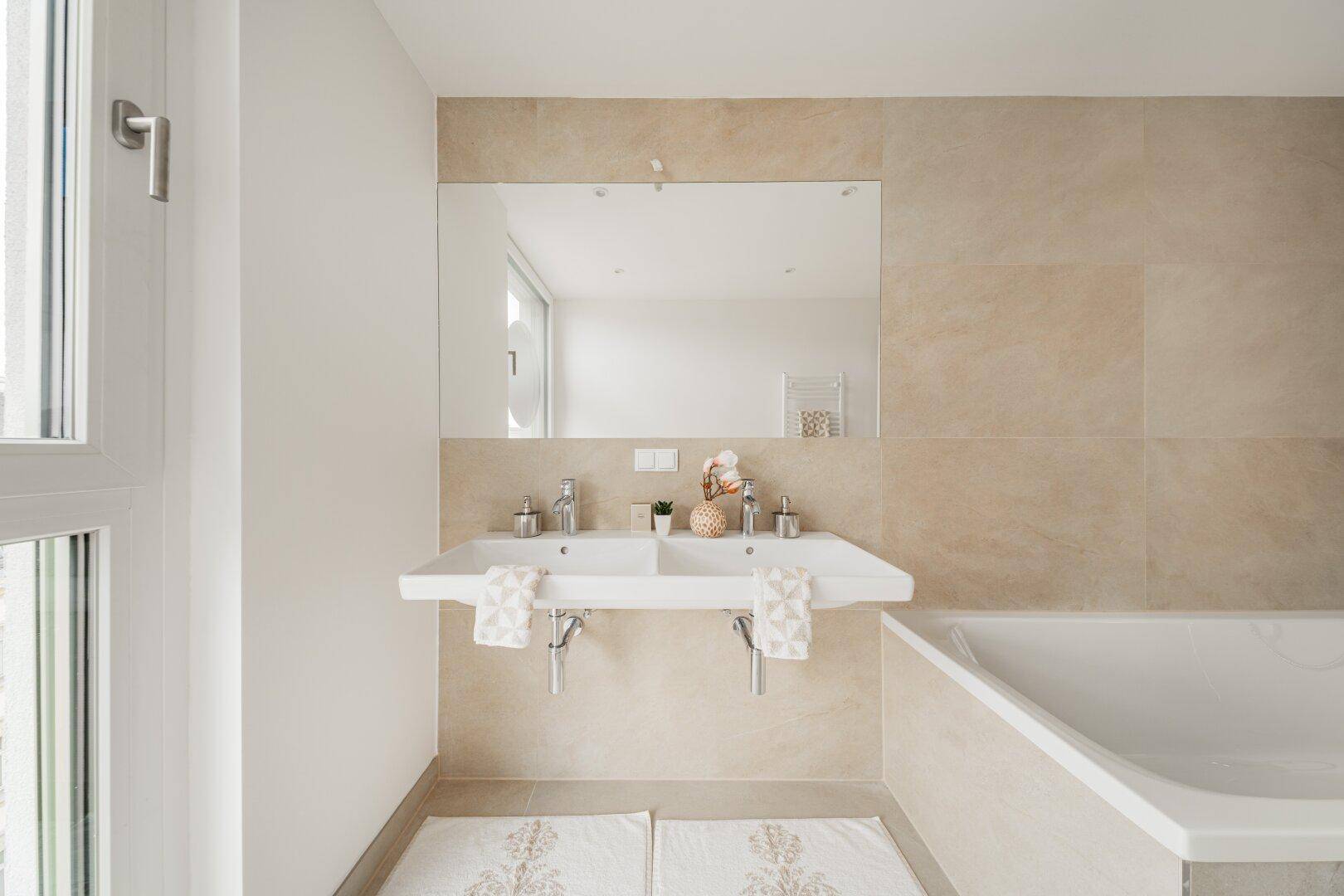 Modernes Badezimmer mit Doppelwaschbecken, großem Spiegel und beigen Fliesen.